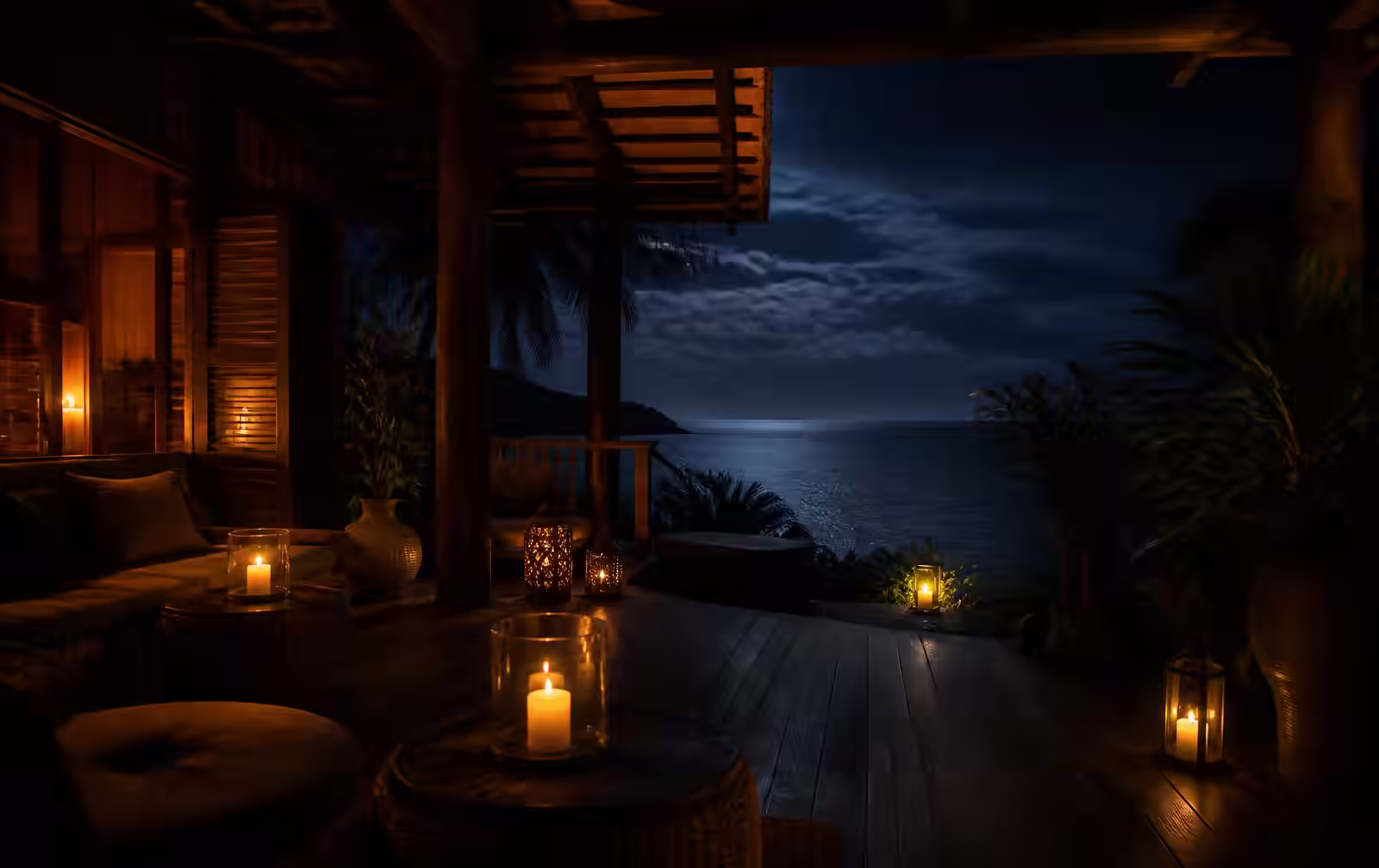 A candlelit timber terrace of a tropical villa looking out over dark night ocean