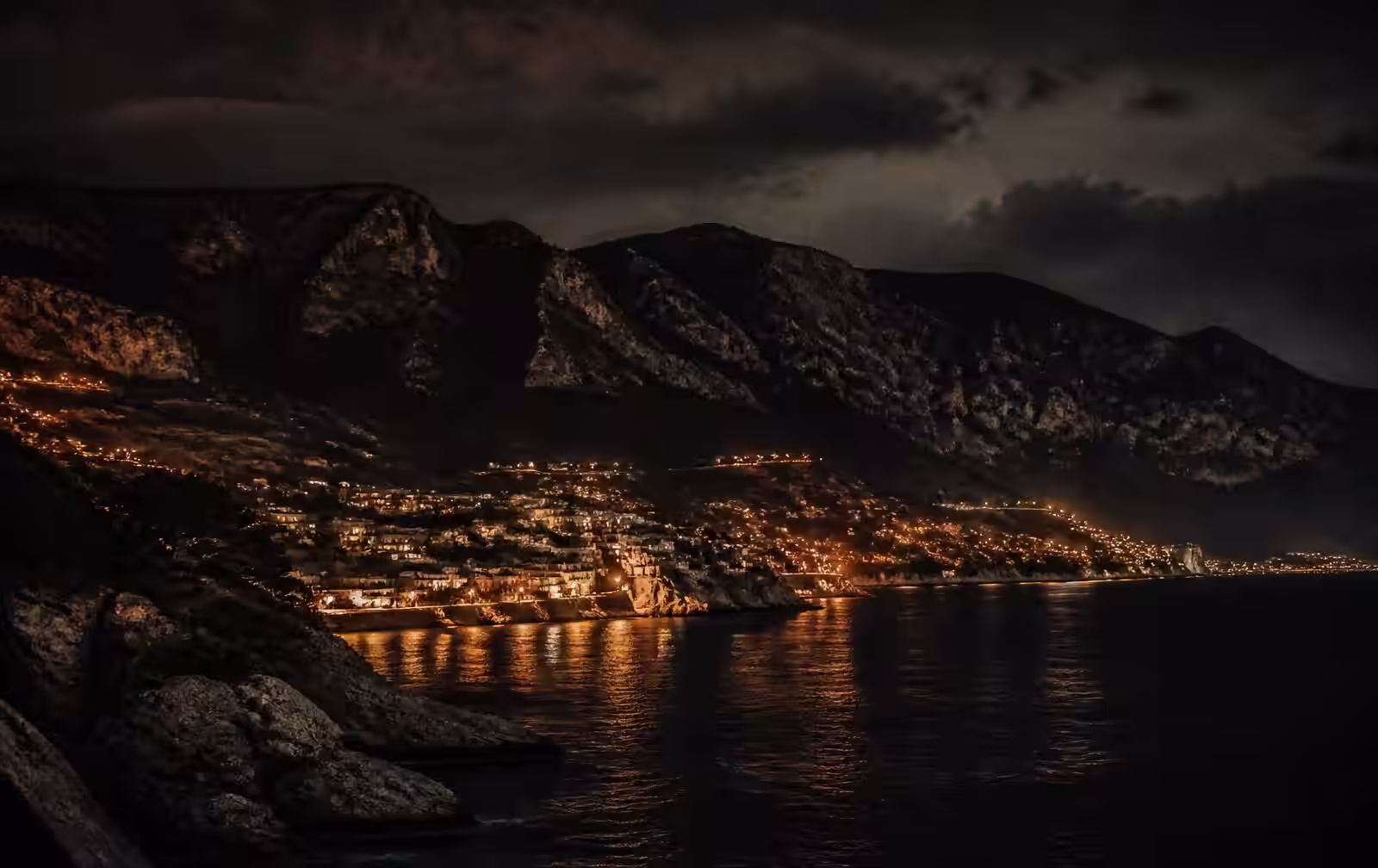 Northern Cyprus coastline at night with a dark mountain ridge and scattered warm town lights above the sea