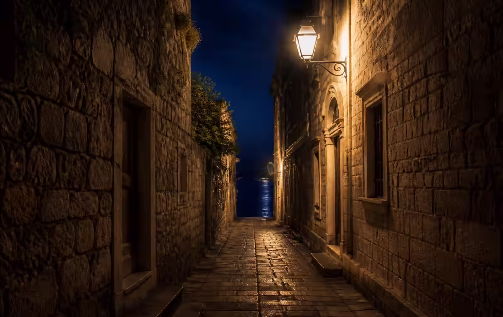 A lantern-lit stone lane in Korčula's old town at night, ending in a glimpse of dark sea