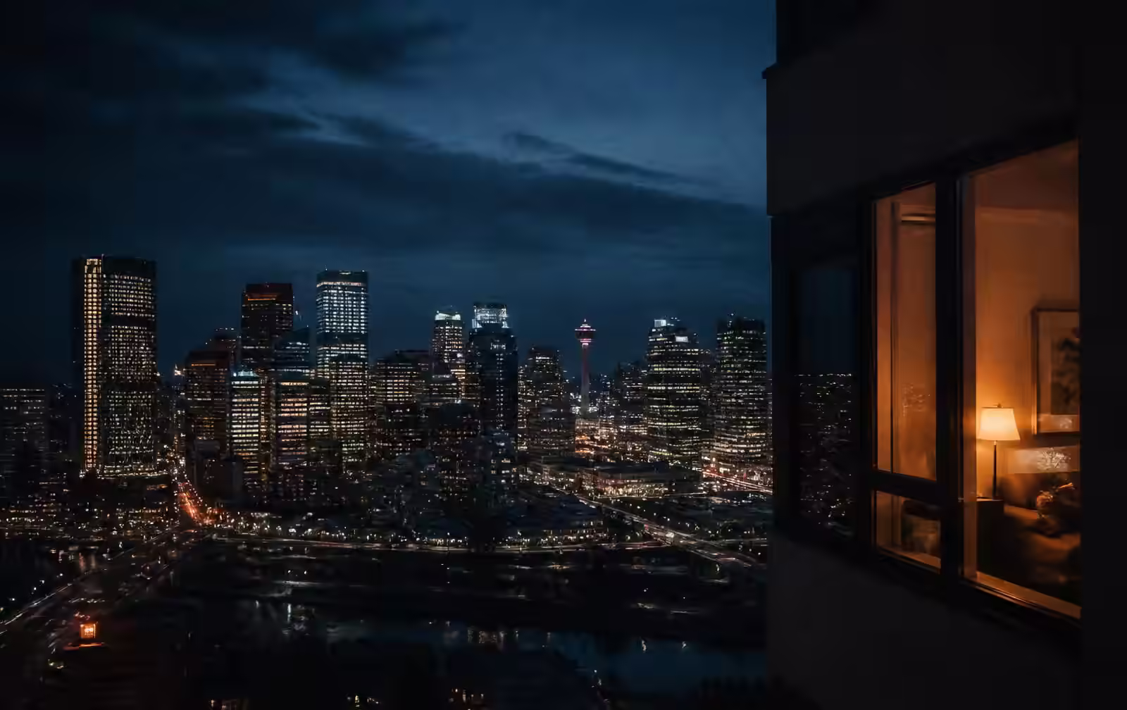 Calgary skyline at night under a wide dark prairie sky with warm light from a high window in the foreground