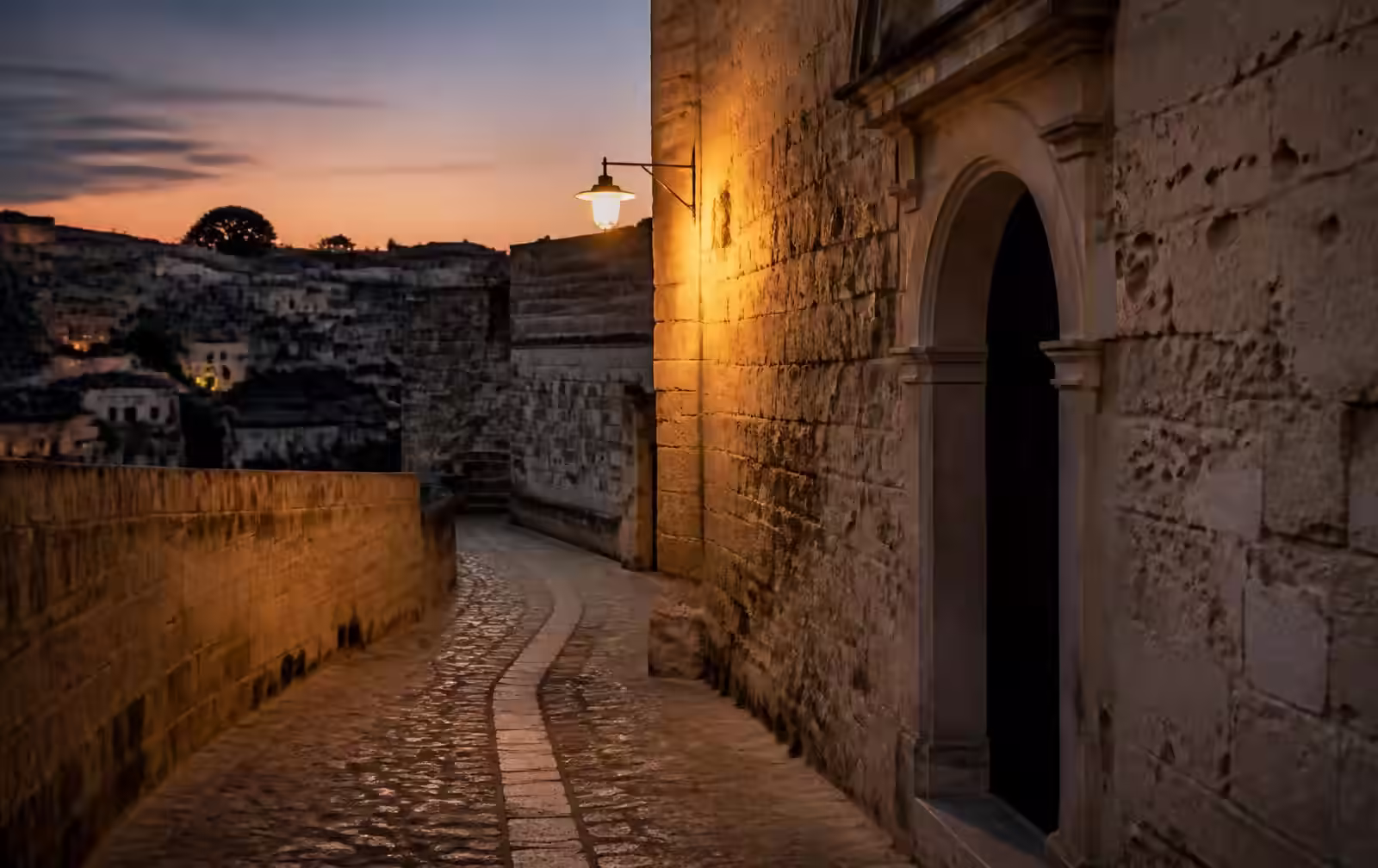 Empty pale limestone street in an old hill city at dusk, warm lamplight on weathered stone walls and a shadowed arched doorway