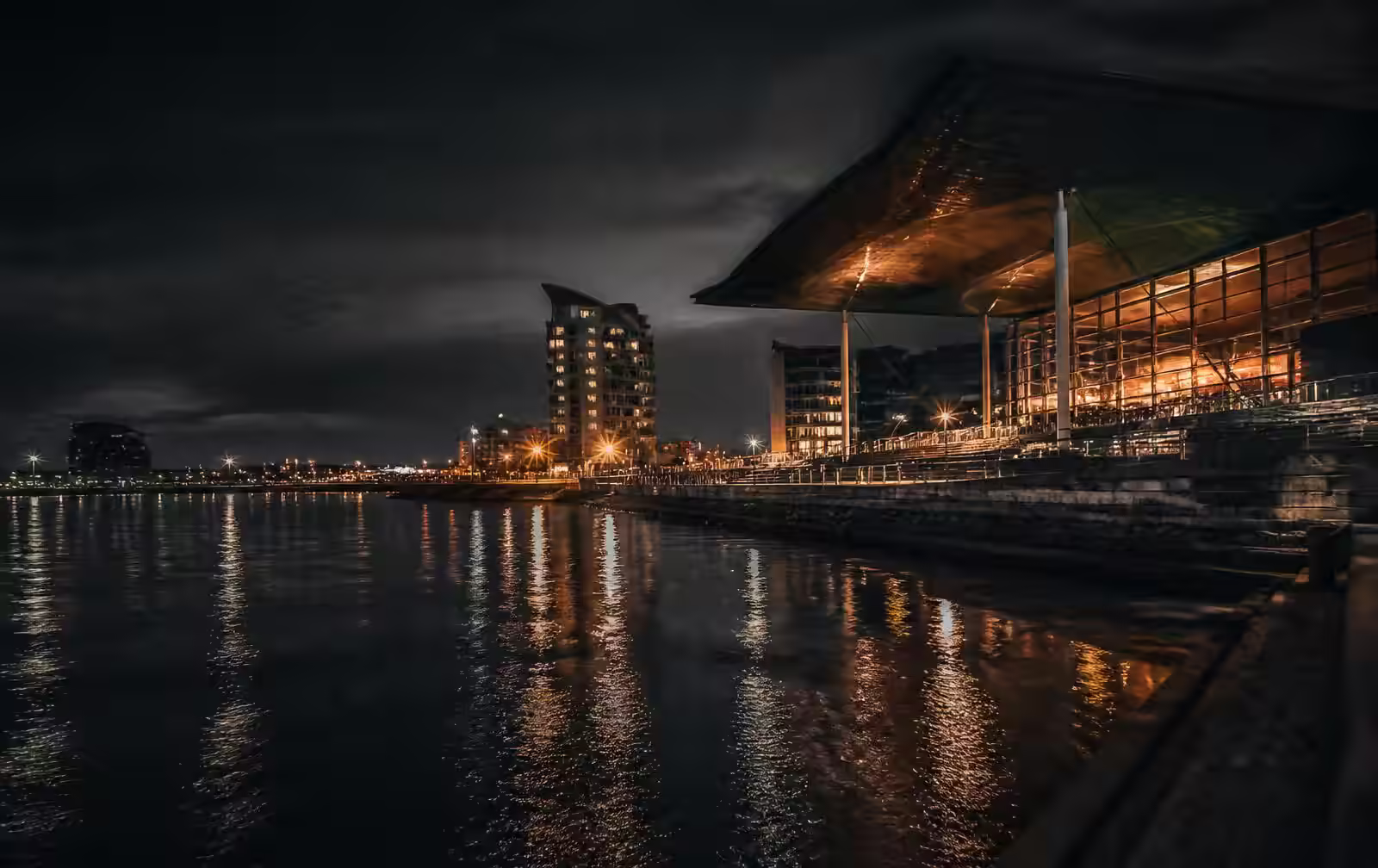 Cardiff Bay waterfront at night with dark water and warm light from modern architecture