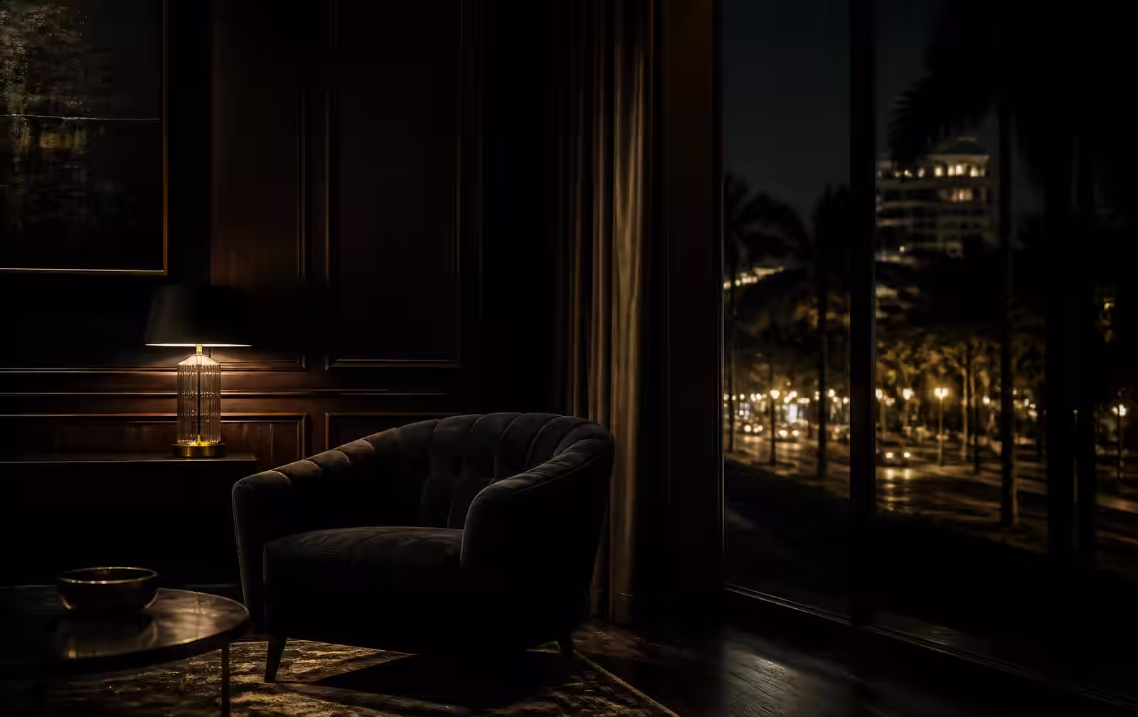 A dark wood-panelled hotel lounge lit by a single warm lamp, with a tall window looking onto a tree-lined boulevard at night