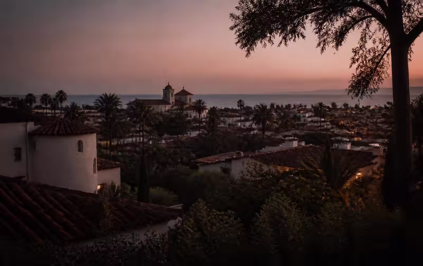 Santa Barbara waterfront at dusk with a private terrace lit warmly above the Pacific
