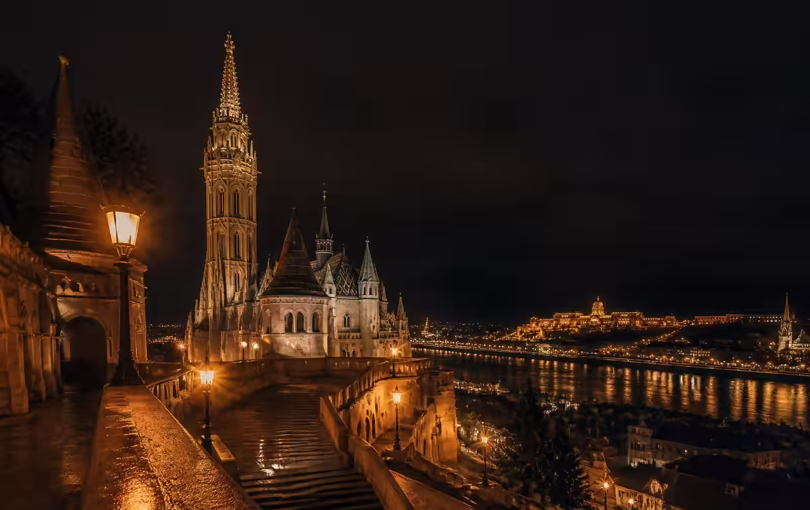 An elegant Central European city at night with a lit cathedral spire and a fortress above the Danube