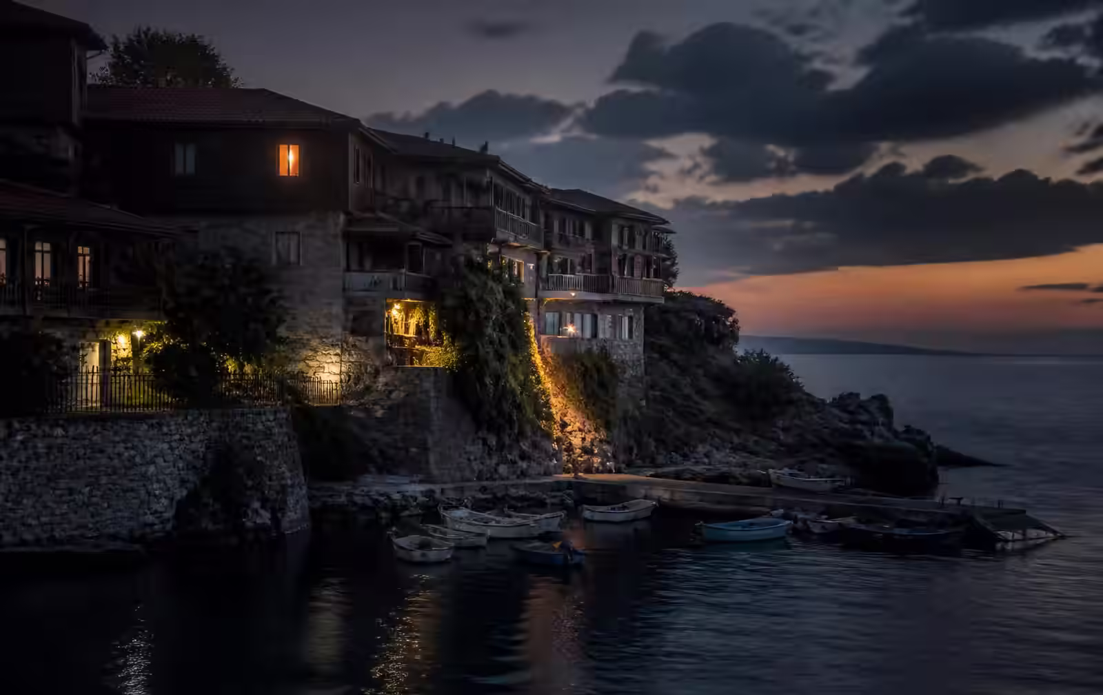 Sozopol's old stone and timber houses above the harbour at dusk, one window glowing warm