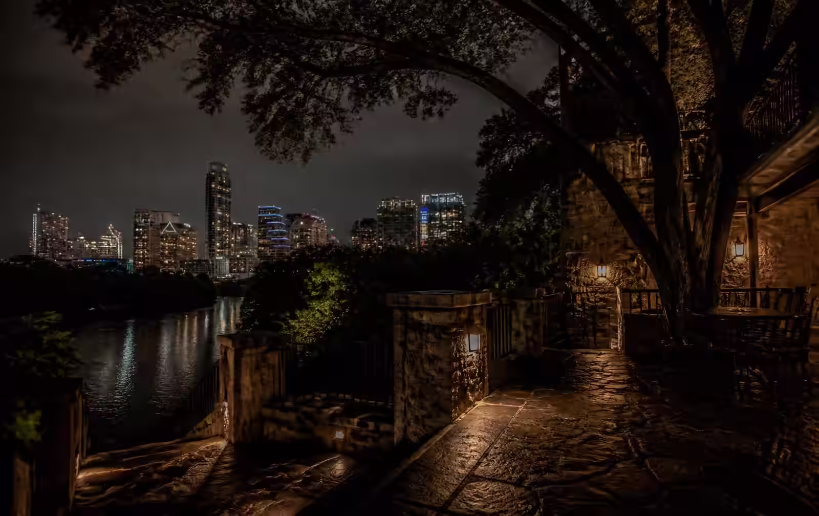 A quiet, dimly lit Austin loft interior at night with the downtown skyline glowing softly through a window