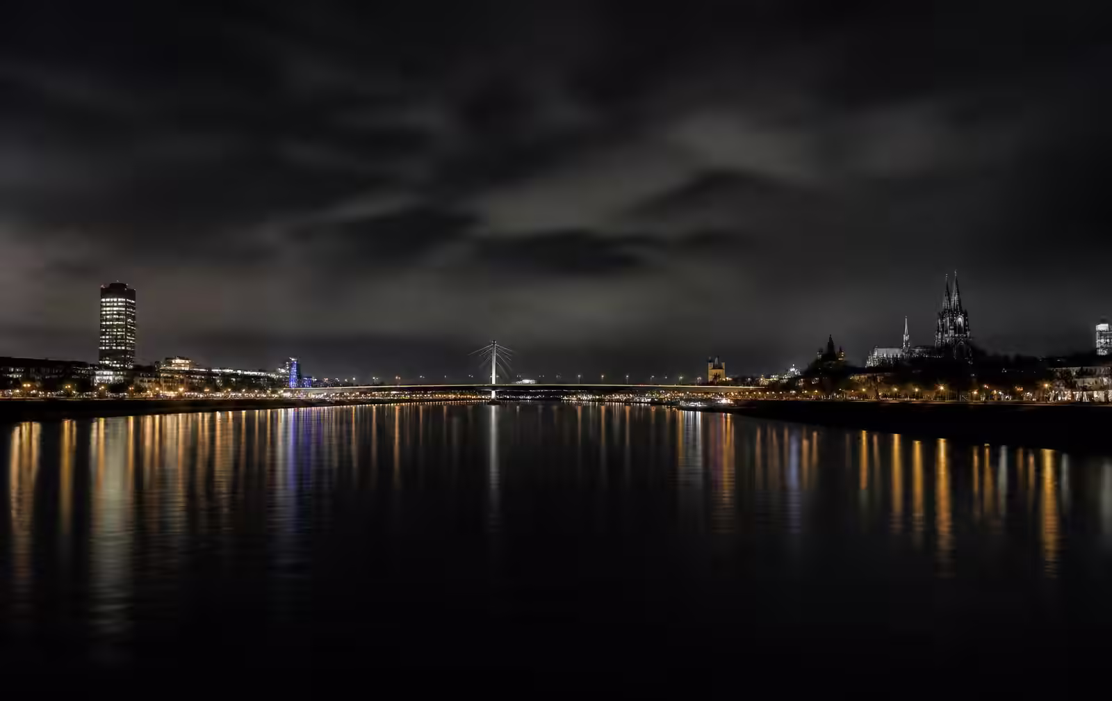 The Rhine at night with city lights and a bridge reflected across black water under a heavy sky