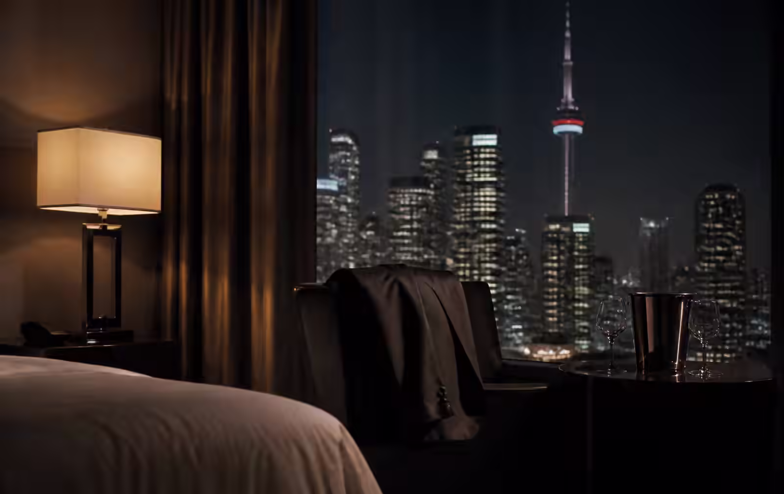 Dark Toronto hotel room at night with a low lamp and the lit downtown skyline beyond the glass