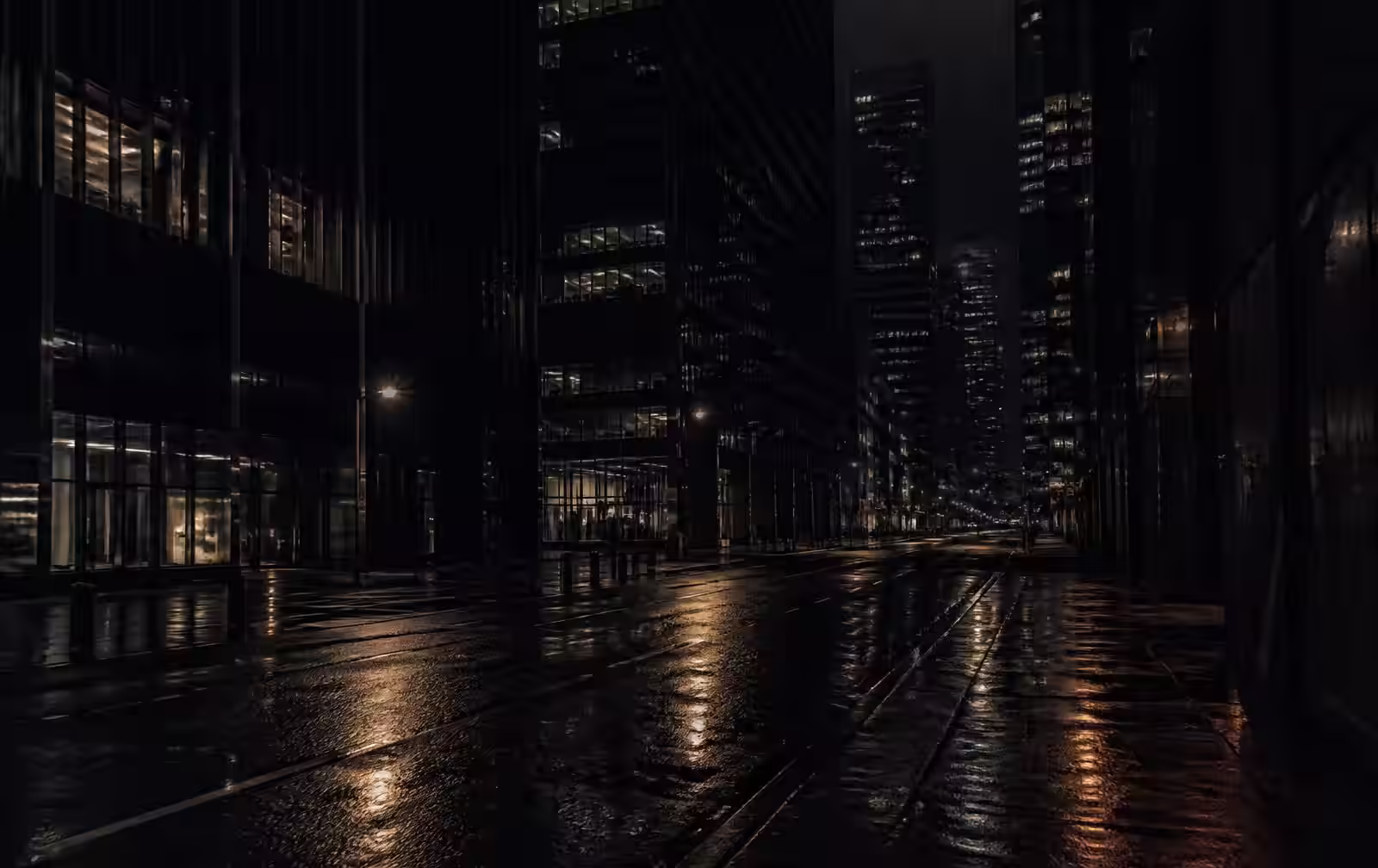 An empty financial district street after rain at night, glass towers with scattered lit windows reflected on wet asphalt