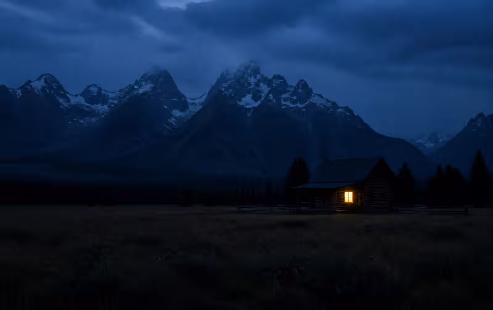 Alberta at night with prairie giving way to dark Rocky Mountain peaks and one warm lit window