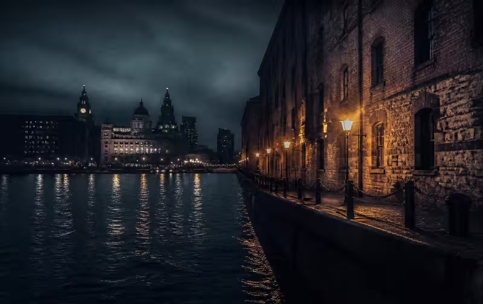 Liverpool waterfront at night with dark river water, dock warehouse stone and distant lit buildings