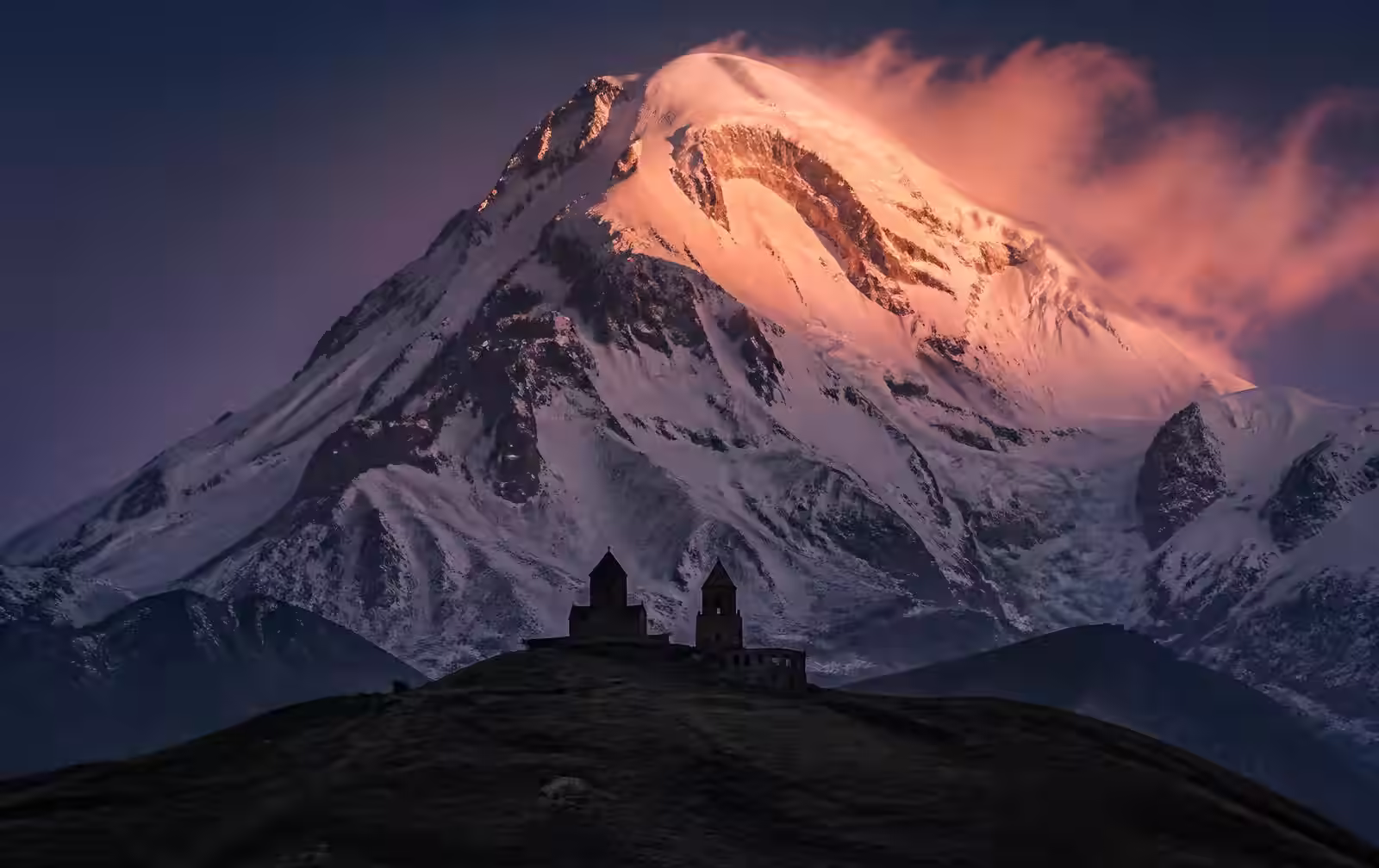 Gergeti Trinity Church silhouetted beneath the snow face of Mount Kazbek at dusk