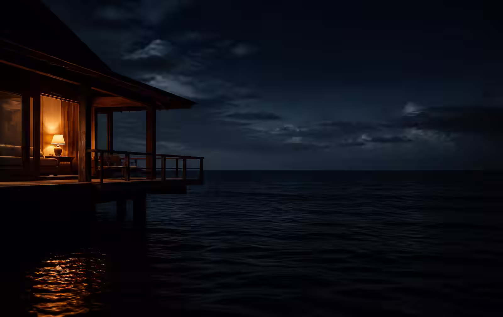A single warm-lit villa terrace on the left edge of a vast dark ocean at night