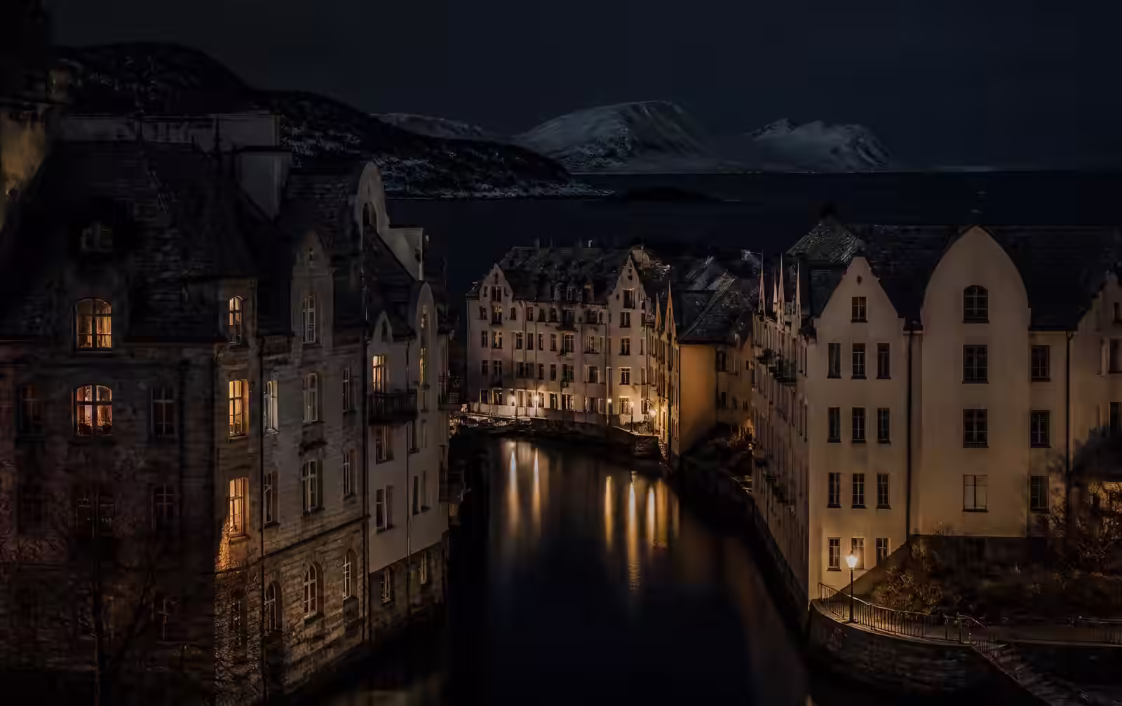 A Norwegian coastal town at night, stone art-nouveau buildings above a narrow dark canal, warm lamplight, snow-dusted islands beyond
