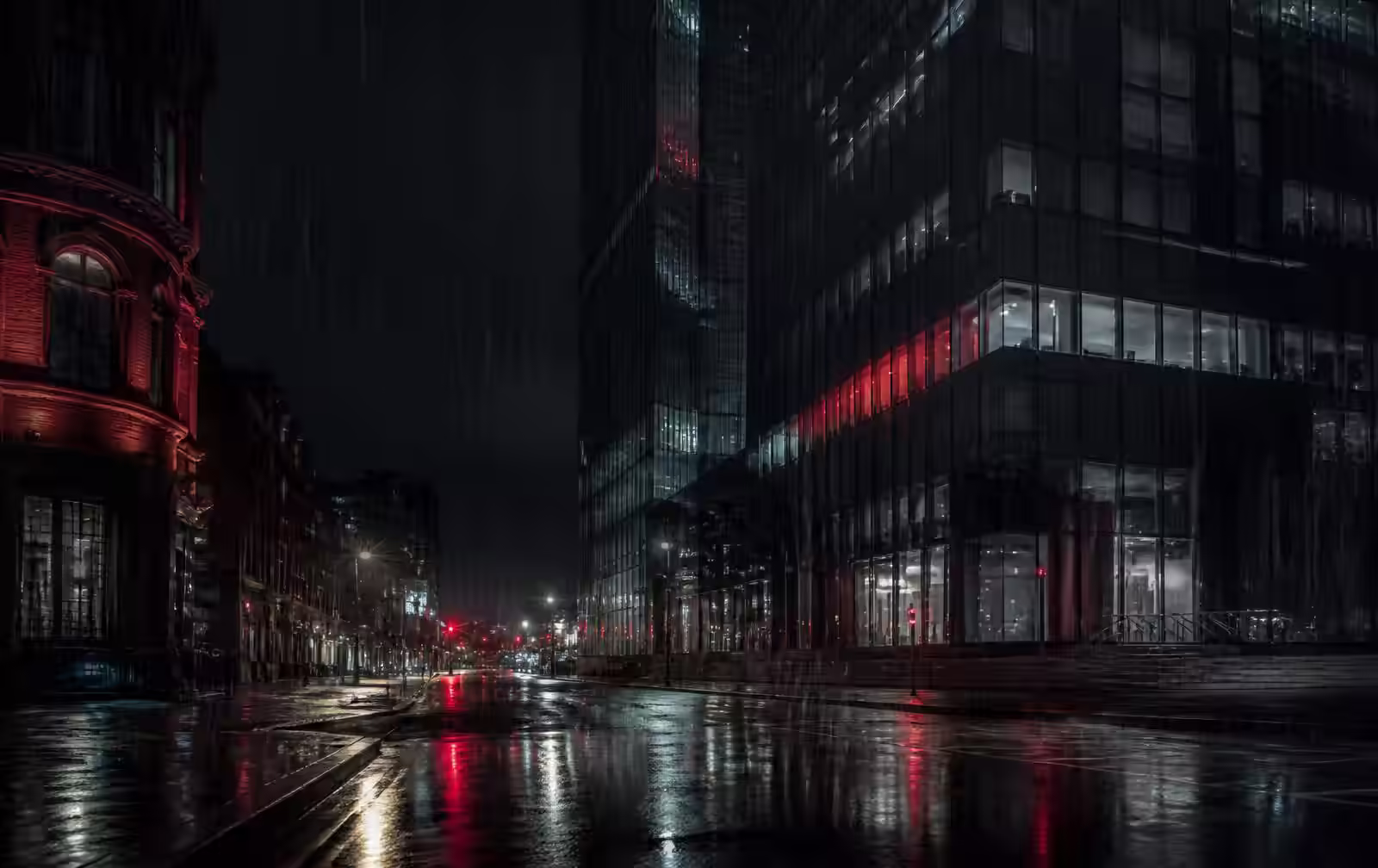 Manchester glass tower and red brick street in heavy night rain with reflections on wet tarmac
