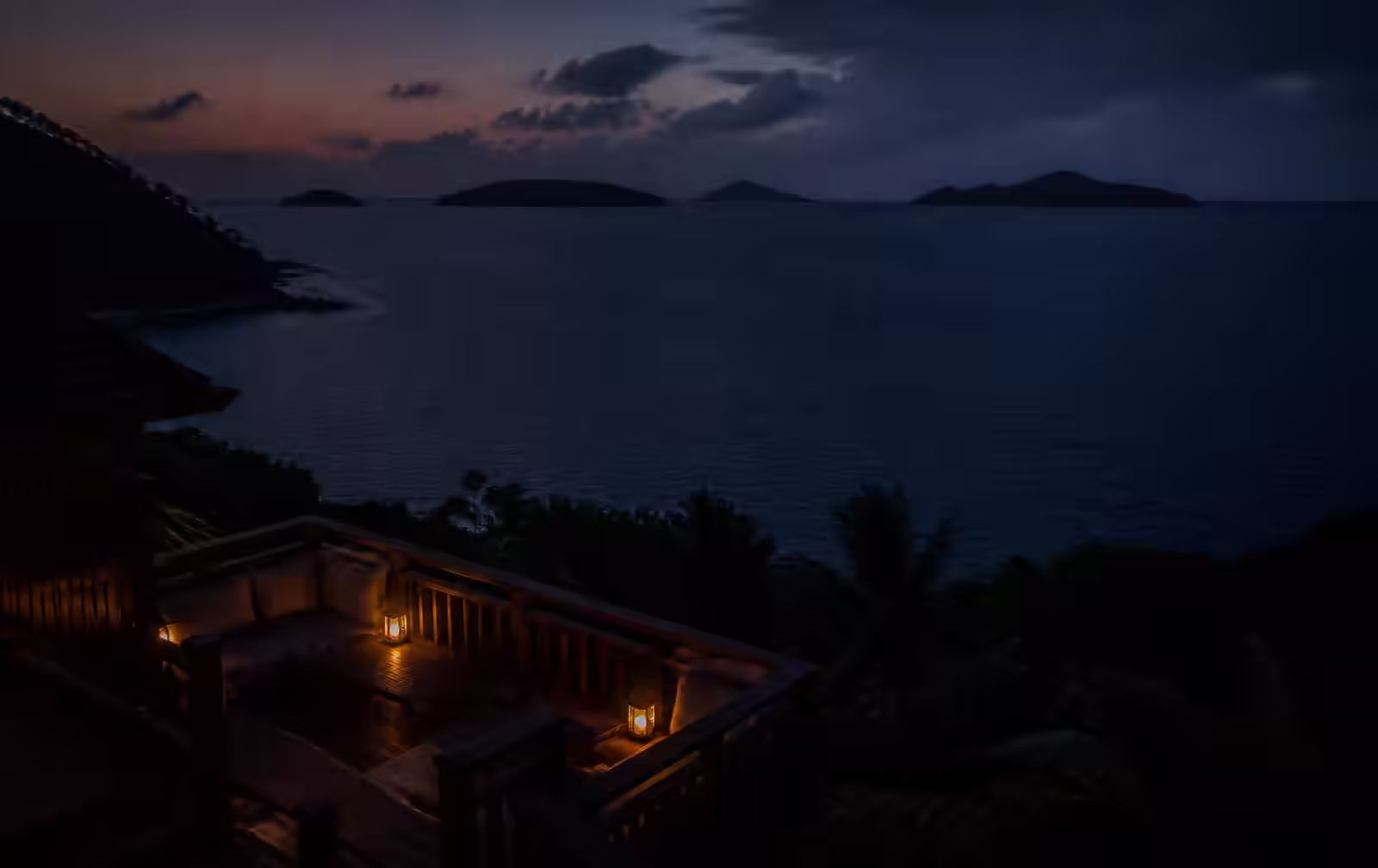 Tropical islands on a dark ocean horizon at late dusk seen from a lantern-lit timber terrace
