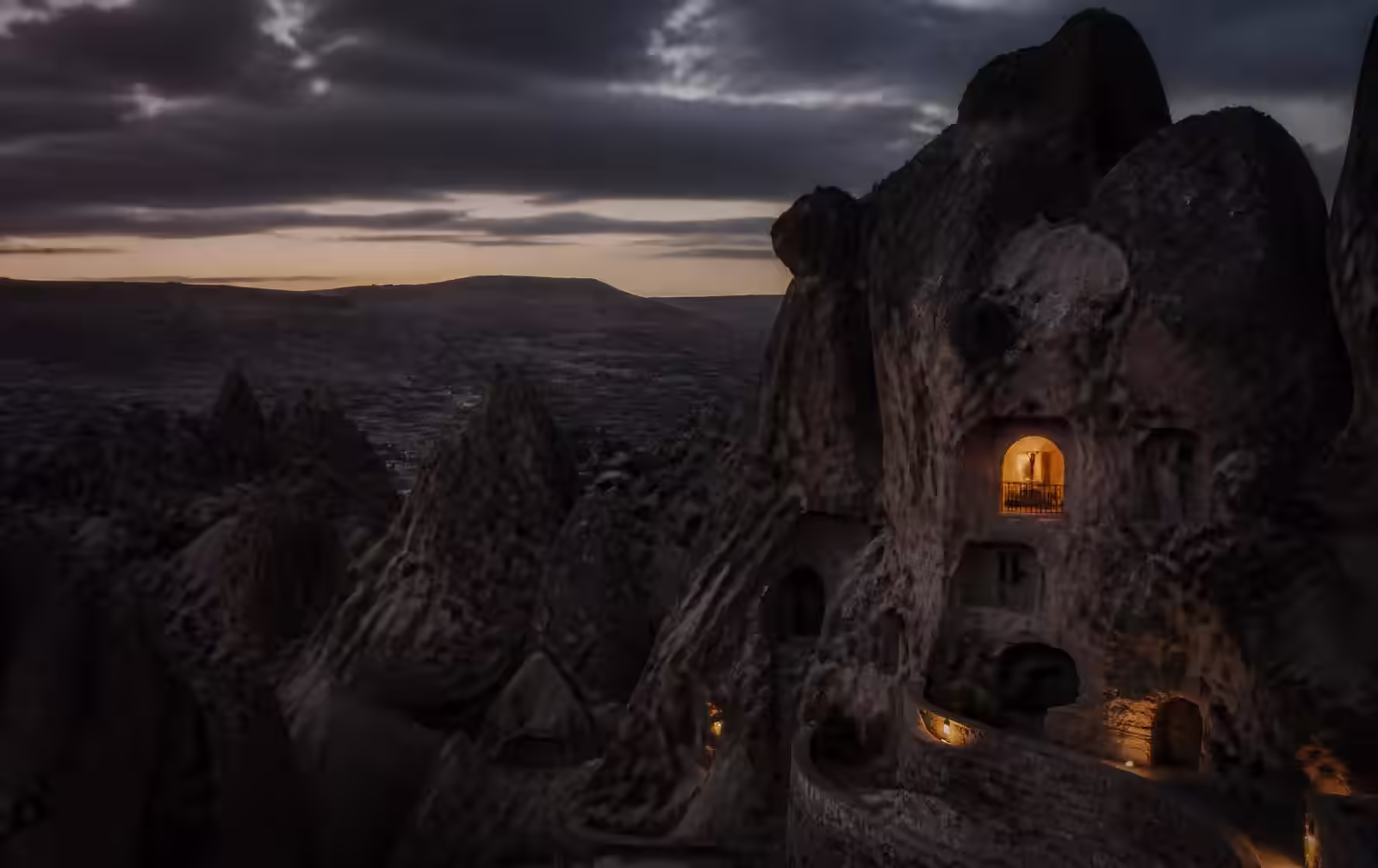 Cappadocian rock valleys before dawn in deep shadow with one warmly lit carved window