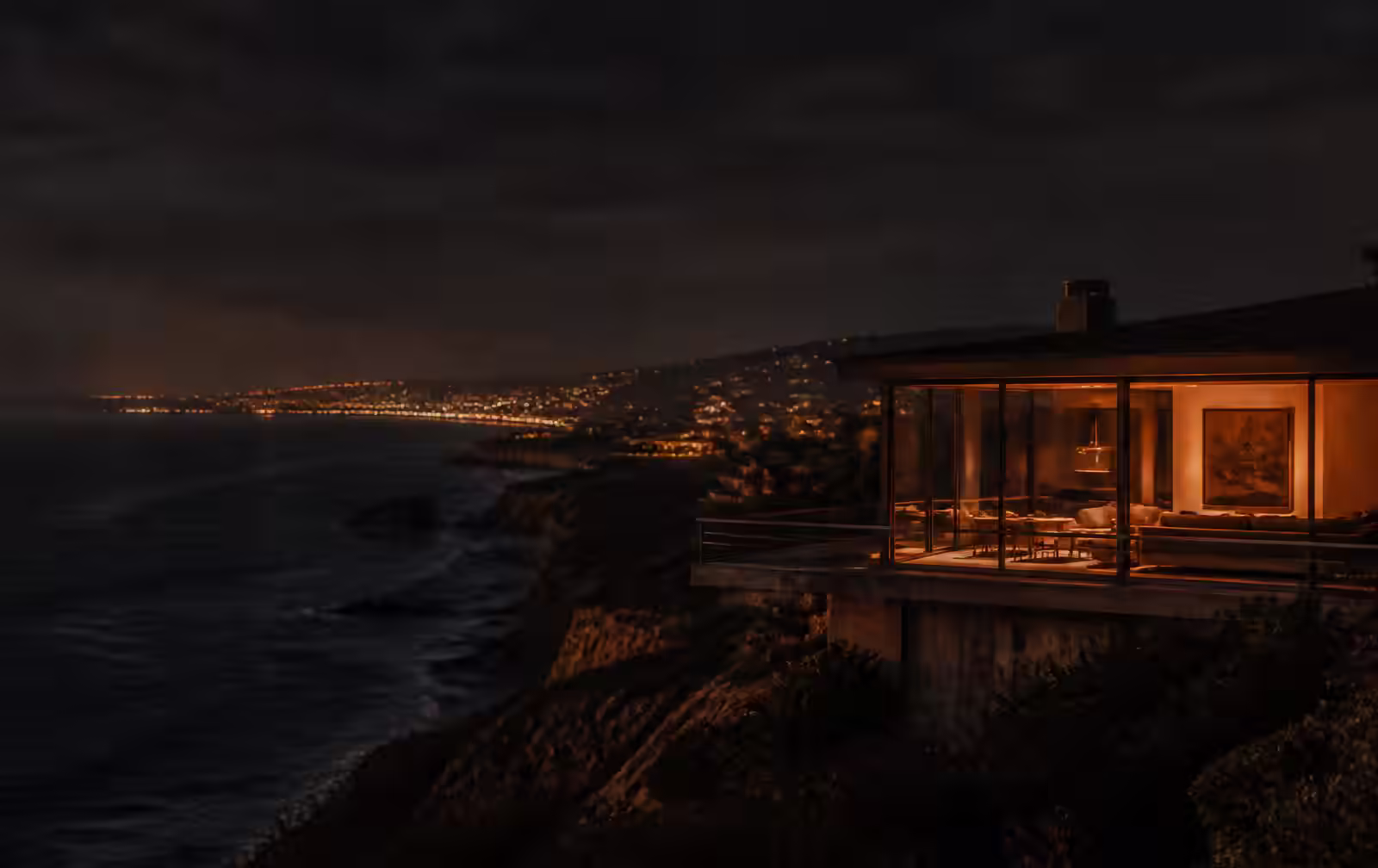 California coastline at dusk with warm light spilling from a private terrace above the Pacific