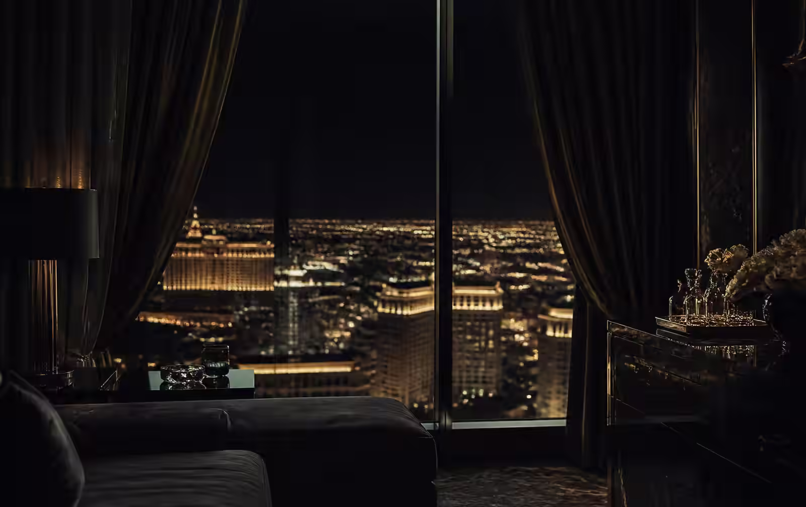High hotel suite window overlooking the glowing Las Vegas Strip at night, the room itself dim and still