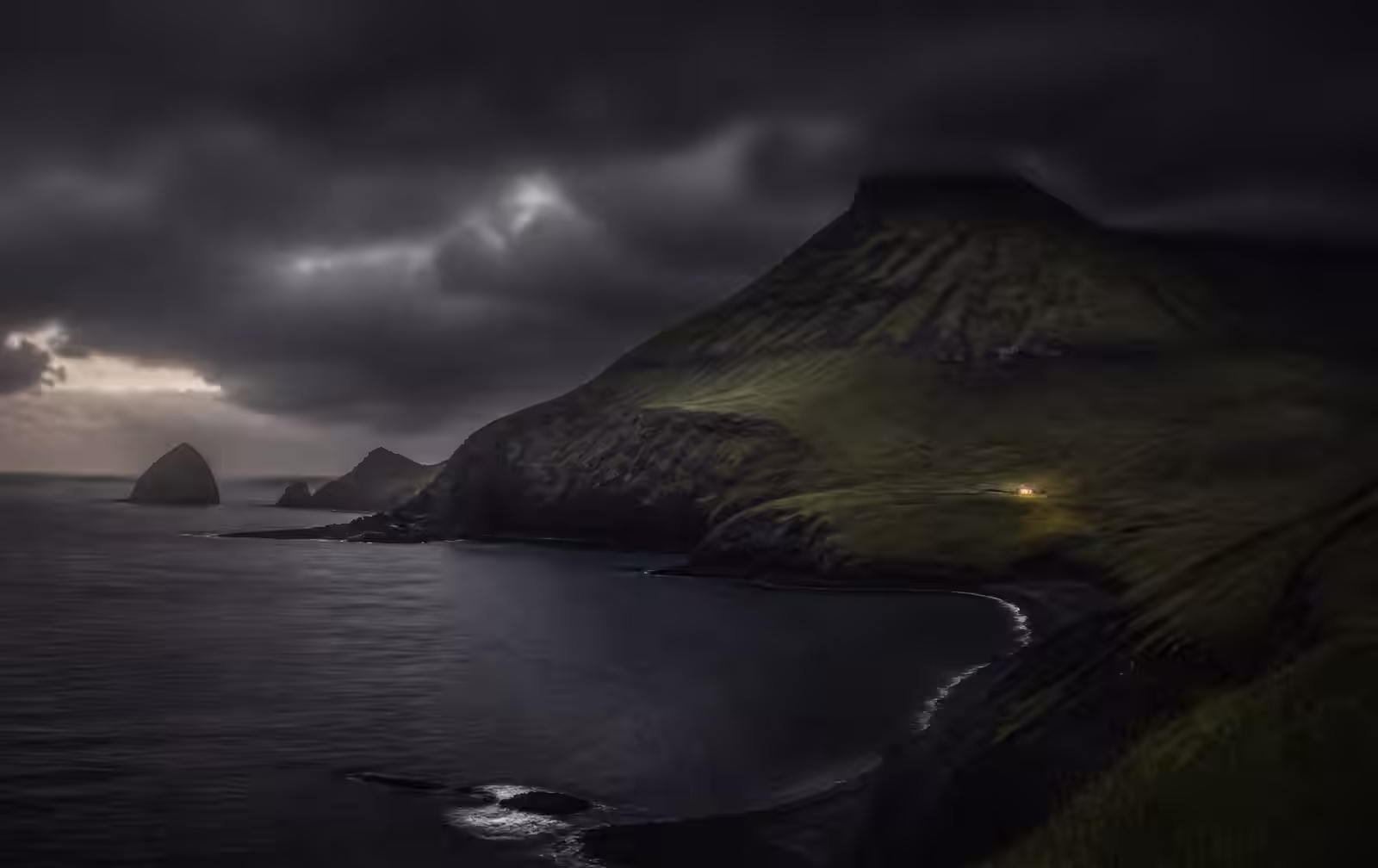 A remote green volcanic coastline under heavy dark Atlantic cloud at dusk