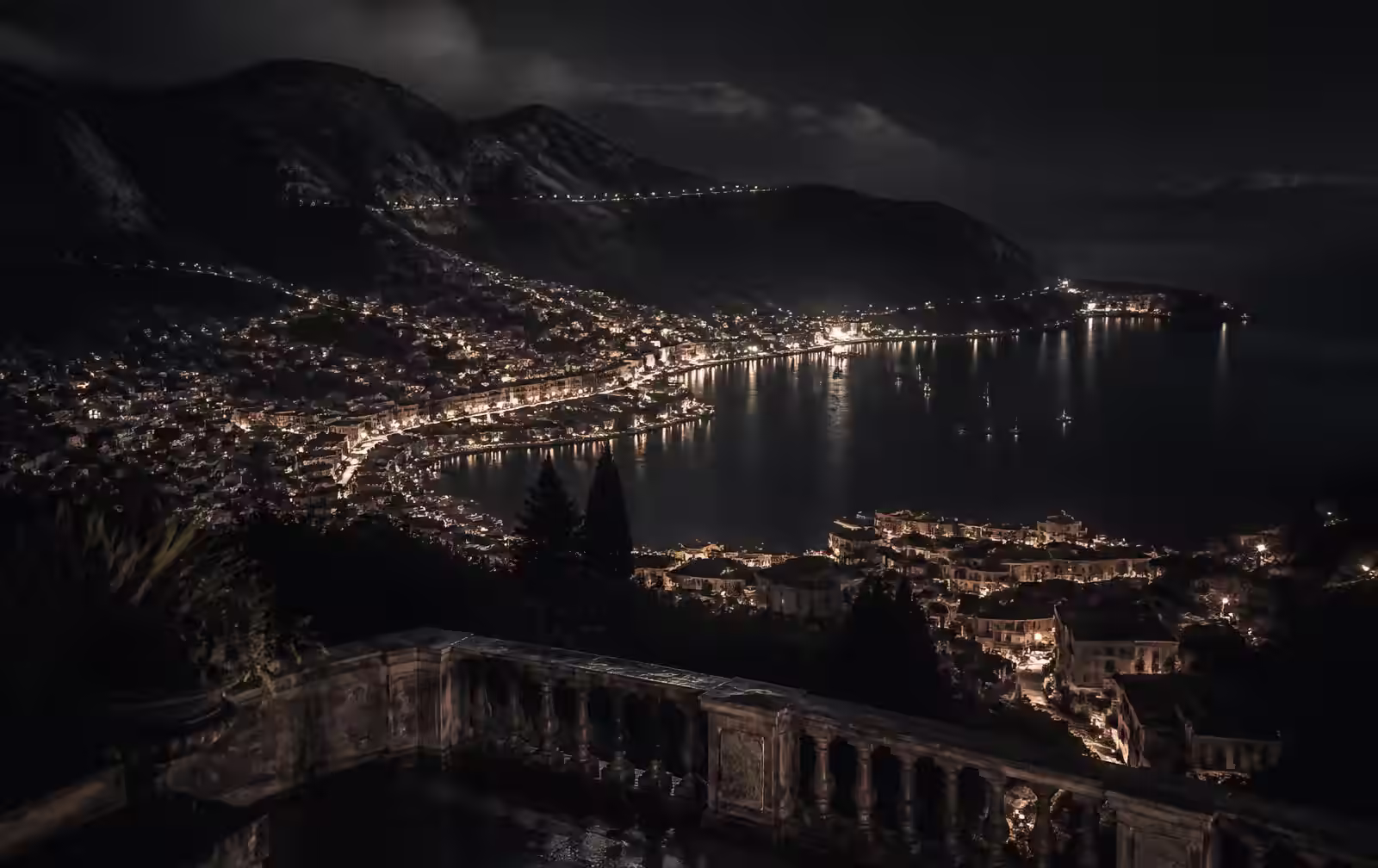 An elevated island city at night with terraced lights descending to a dark bay