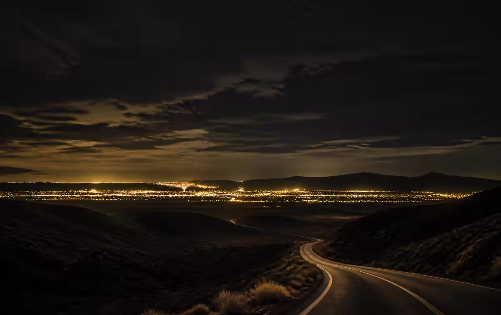 Desert horizon at dusk with distant city lights beginning to glow beneath a darkening sky