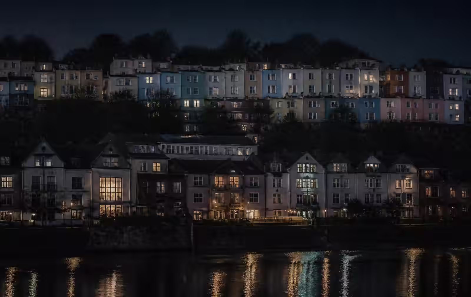 Bristol terraces on the hill at night above dark harbour water with warm lit windows