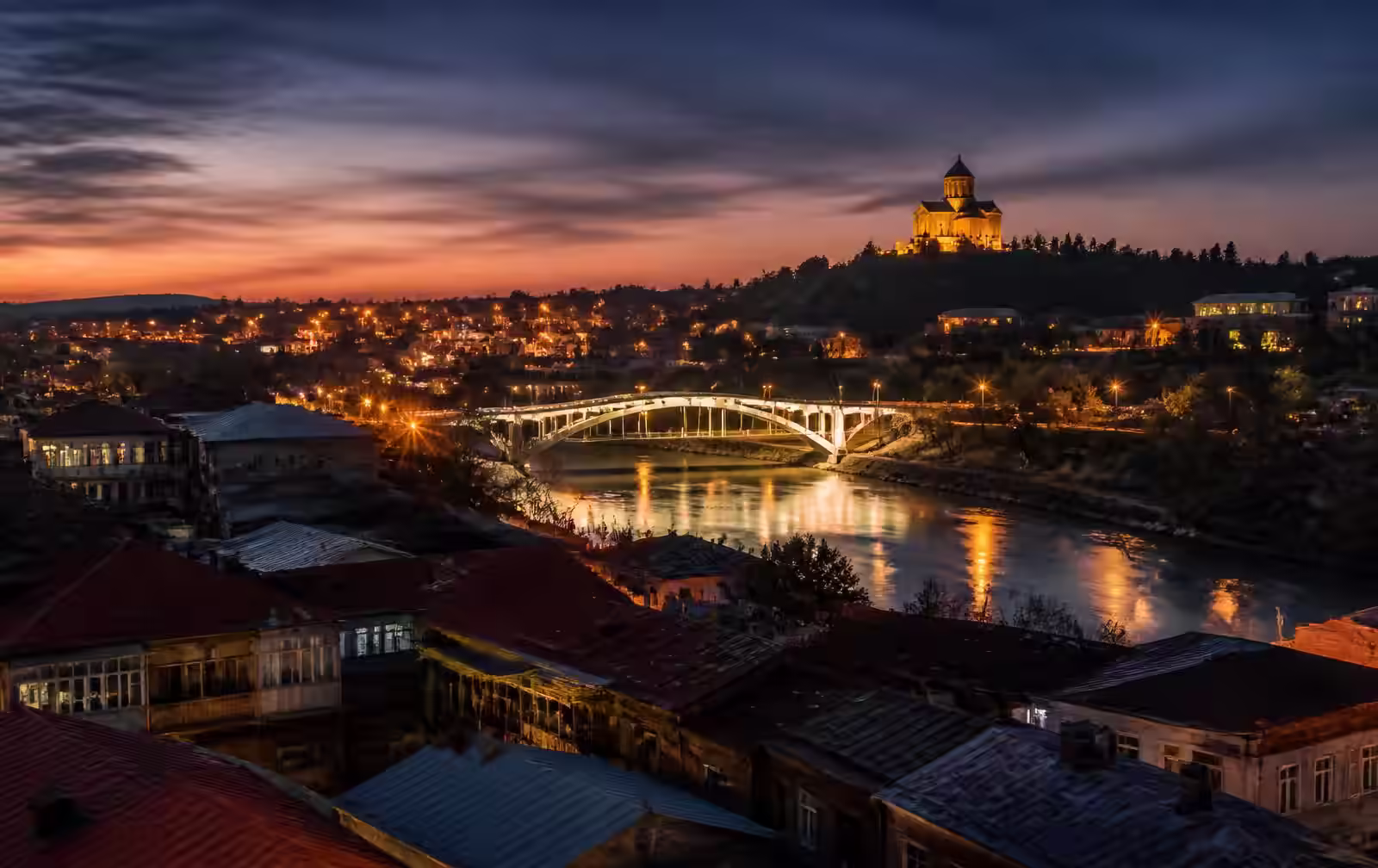 Kutaisi at dusk, the white bridge over the Rioni river and Bagrati Cathedral lit on the hill above old rooftops