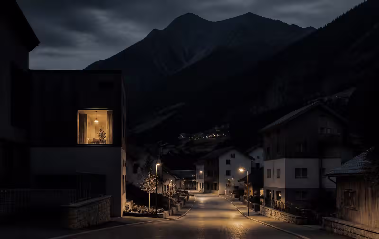 A quiet lamplit street in Schaan at night with one warmly lit window and a dark mountain ridge behind