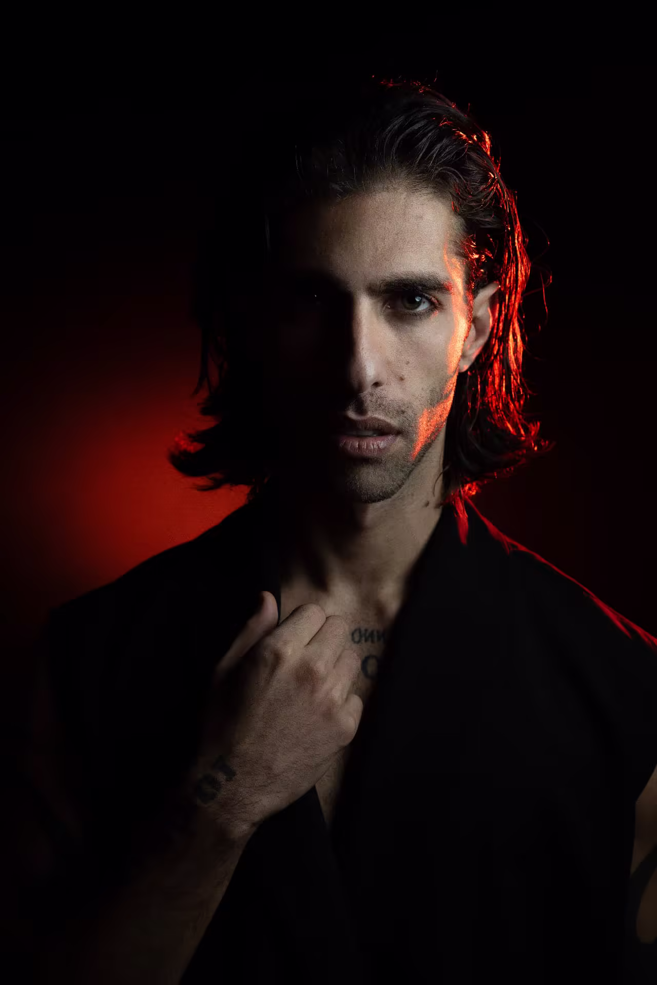 Close portrait of Lucianno Vargas lit by red light, hand at his collar