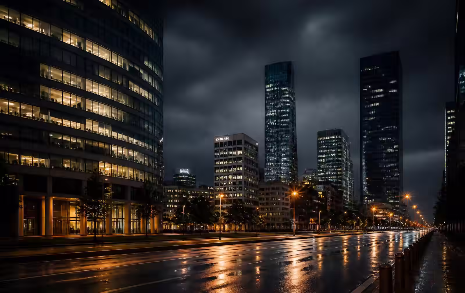 Katowice at night, modern glass and concrete office towers above a wide rain-slicked boulevard, warm window light reflected on wet asphalt
