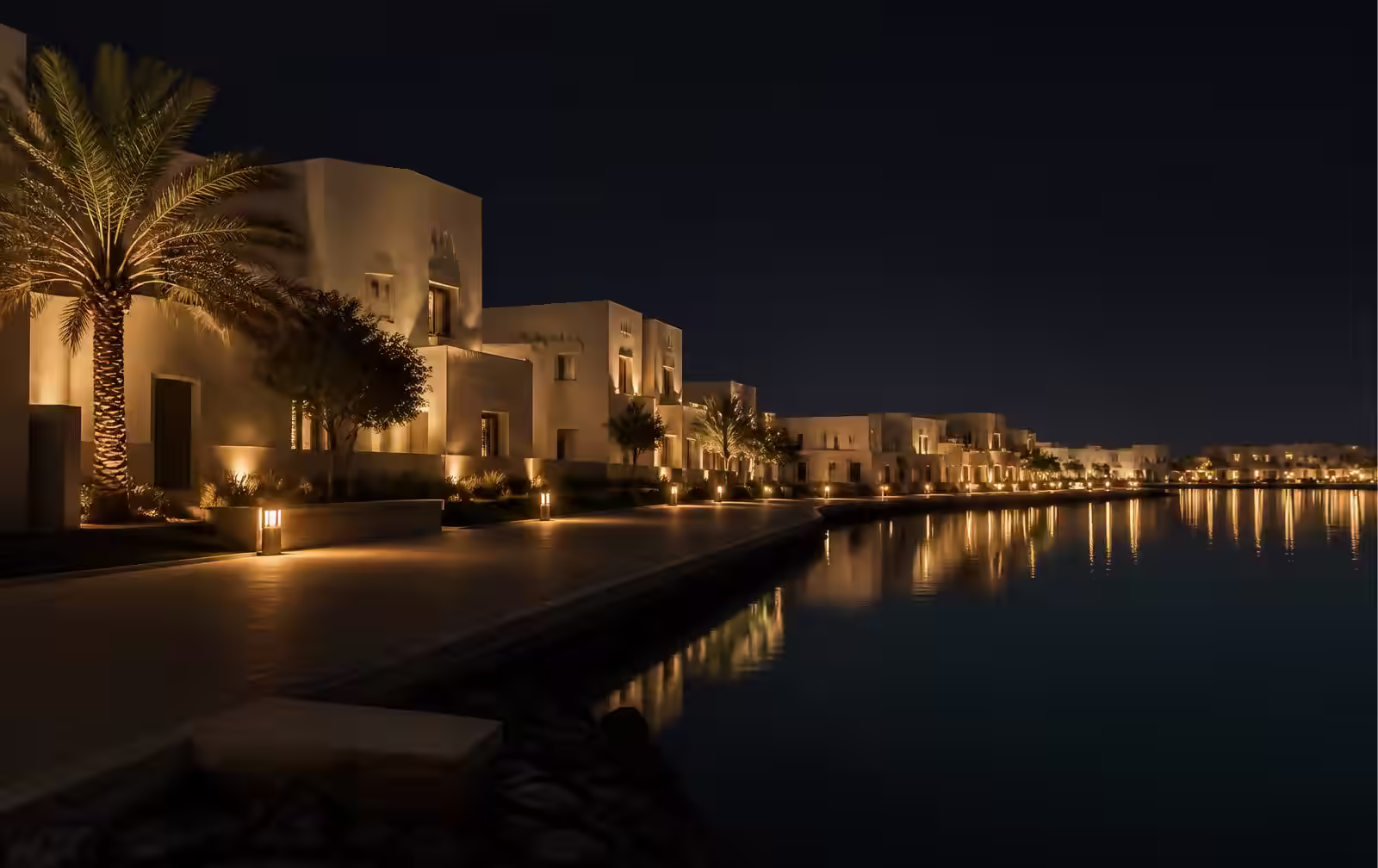 A calm Gulf lagoon waterfront at night with simple ivory architecture and gold lamplight on still water