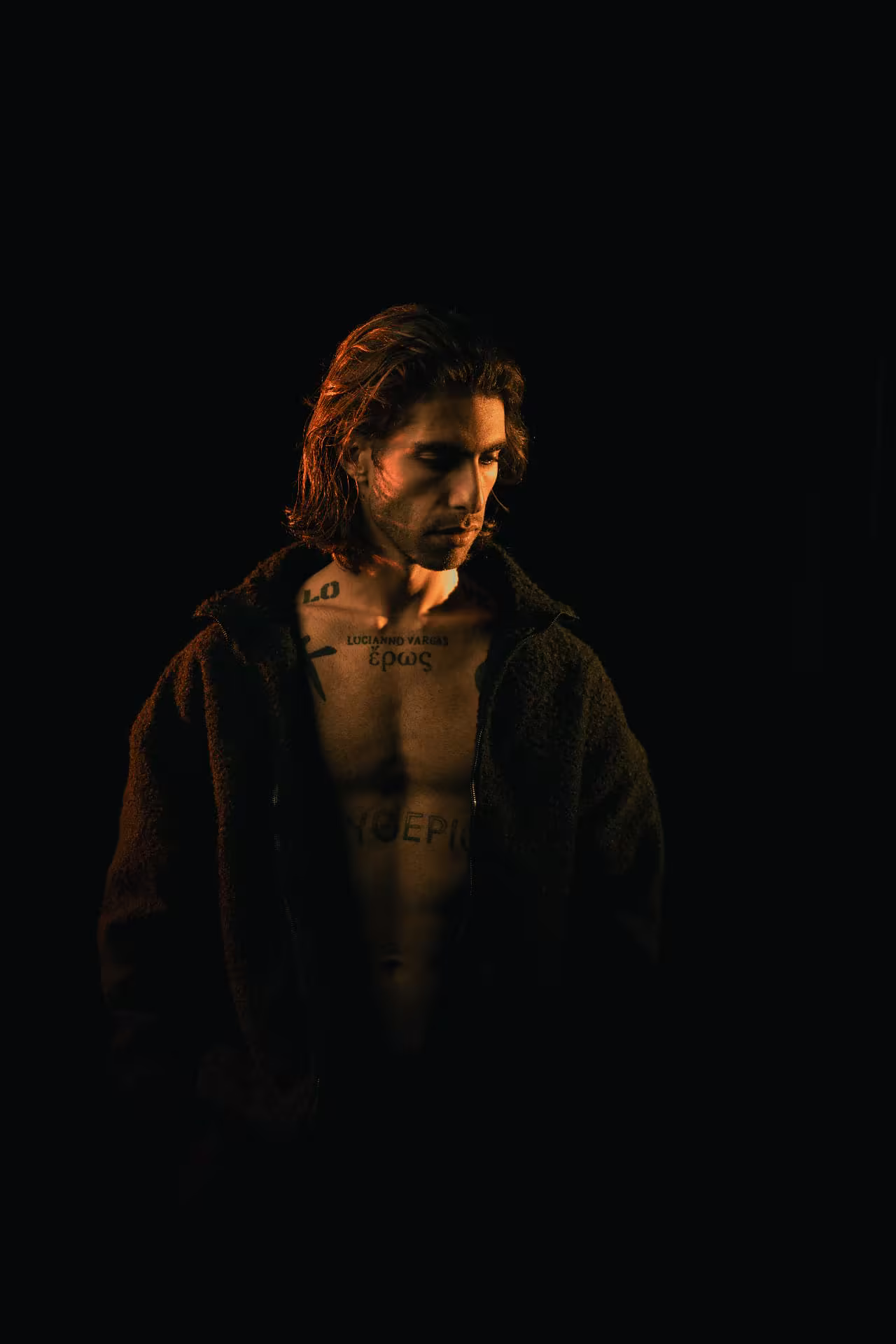Lucianno Vargas in warm amber light, dark jacket open, gaze lowered