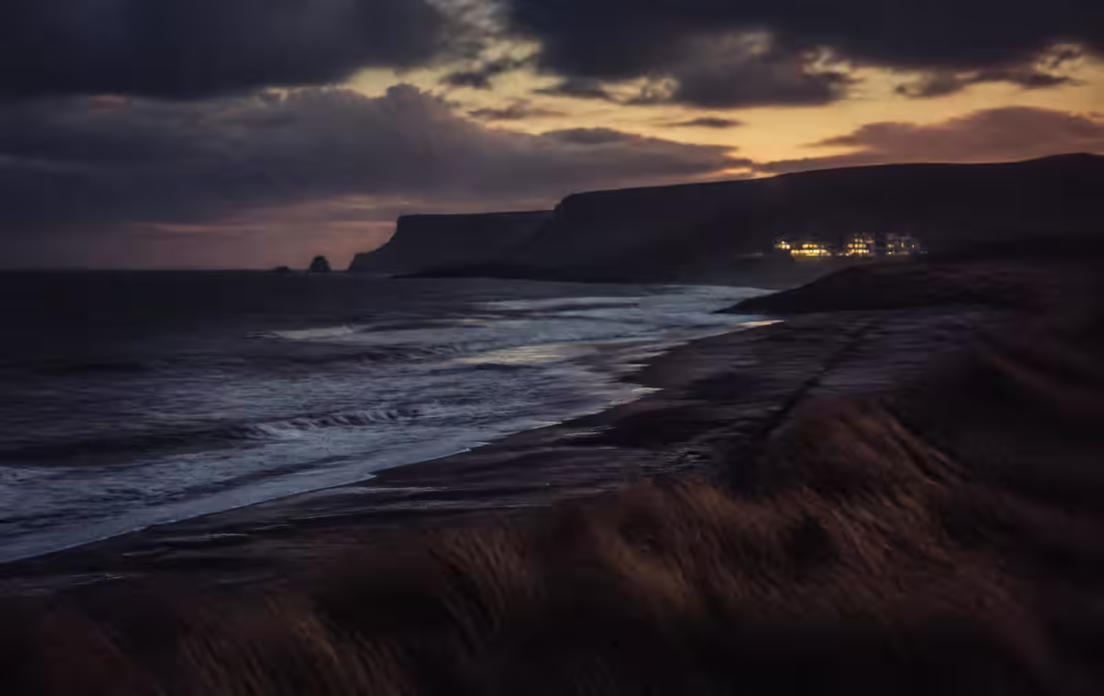North Antrim coast at dusk with dark Atlantic surf, cliffs and a distant lit hotel above the dunes