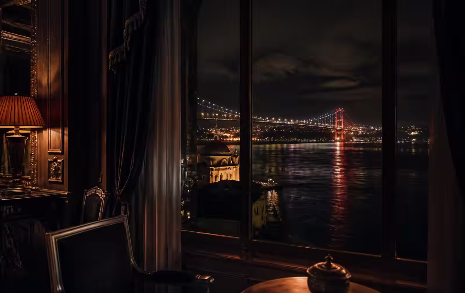 A warmly lit hotel interior with dark wood looking out over the Bosphorus and bridge lights at night