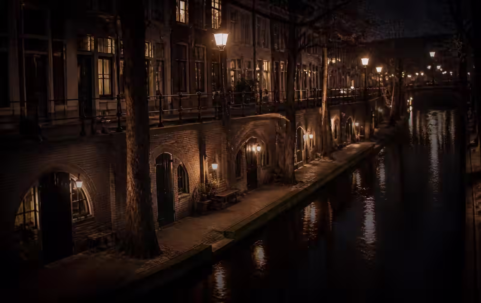 Utrecht canal at night with its lower stone wharf, brick cellar archways along the waterside and warm lamplight