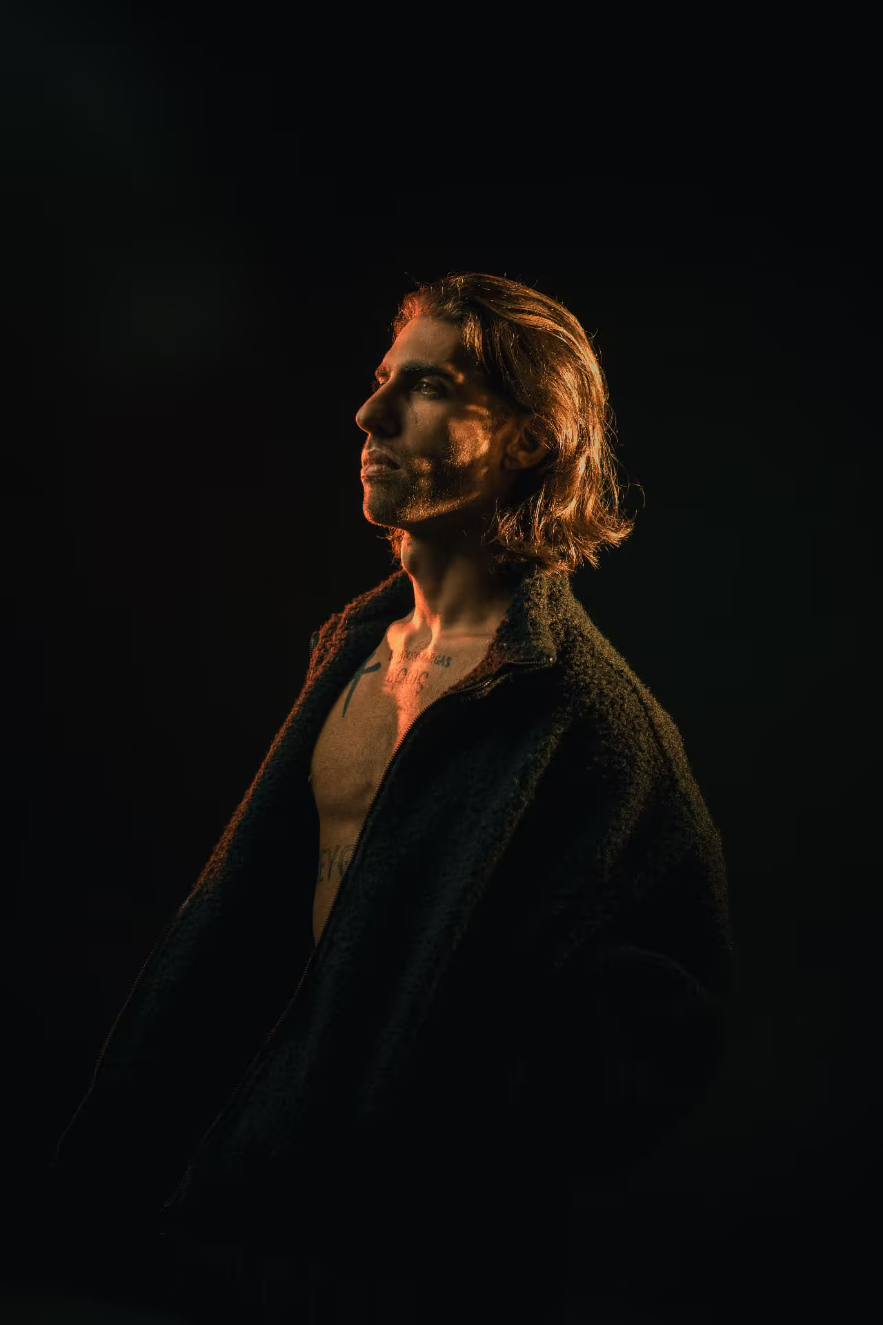 Lucianno Vargas in profile looking upward, lit by a last band of amber light