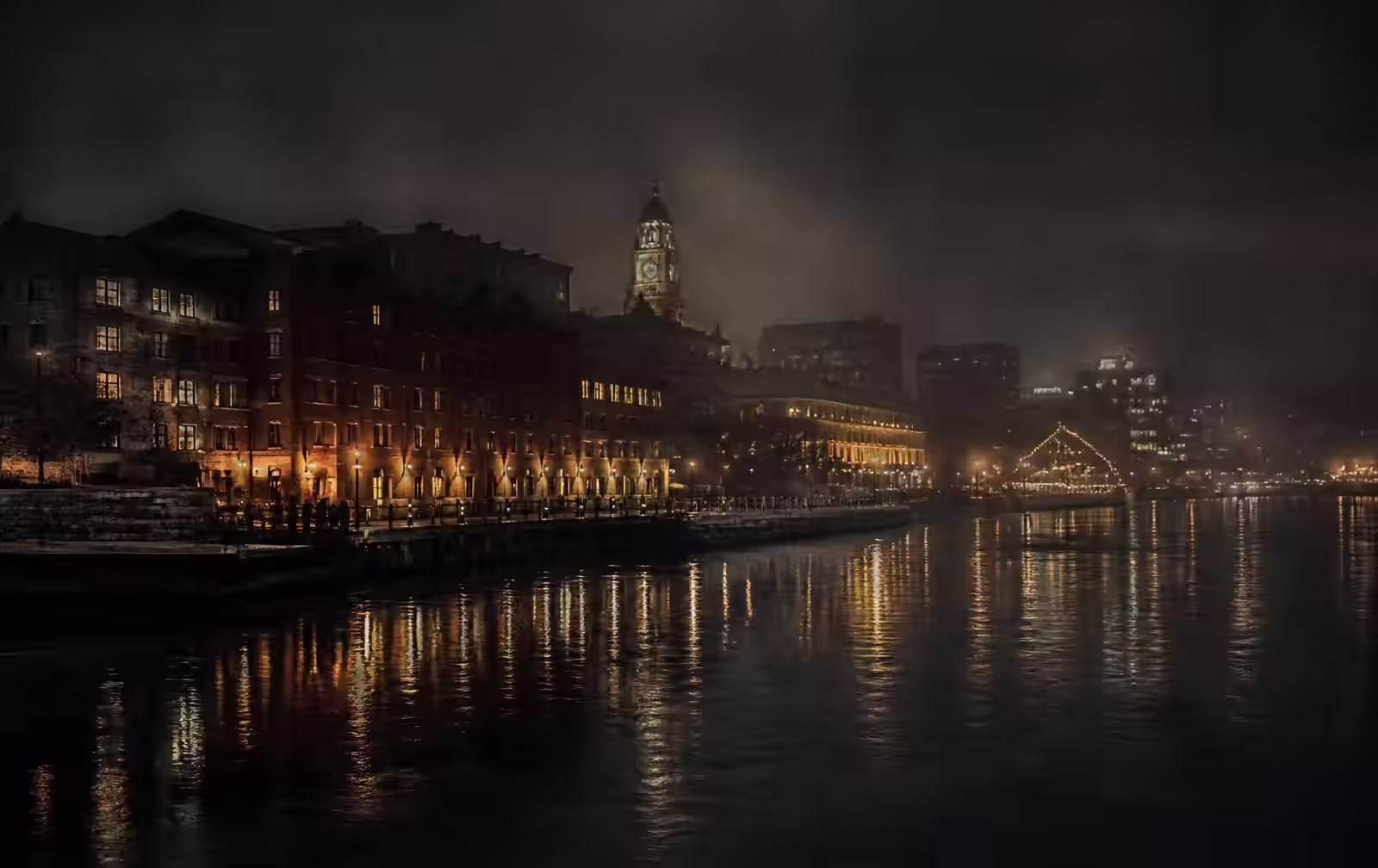 Halifax waterfront at night with warm lights reflected on dark Atlantic water and old brick buildings in mist