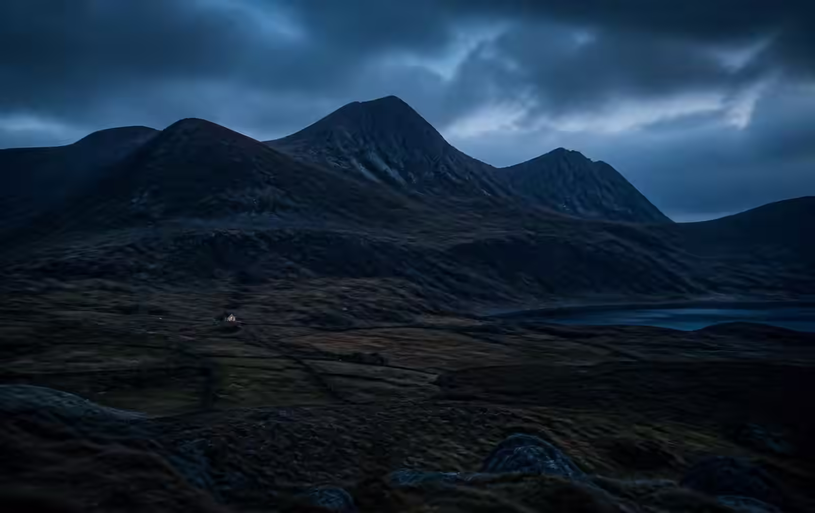 Welsh mountains at blue hour above a dark valley with a single distant lit cottage
