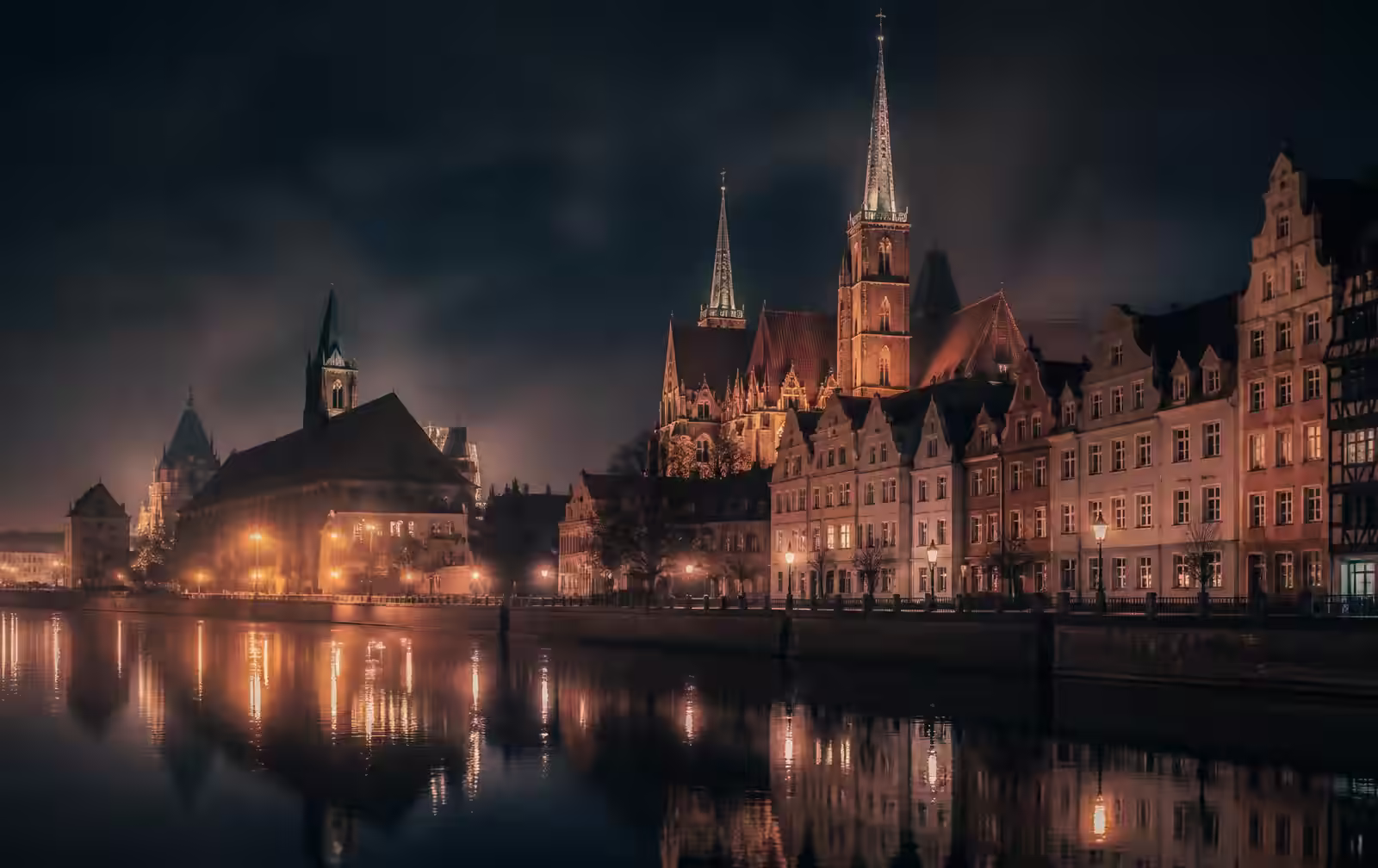 Wrocław market square at night, tall colourful gabled townhouses lit from within, wet cobblestones and an empty square under a dark sky