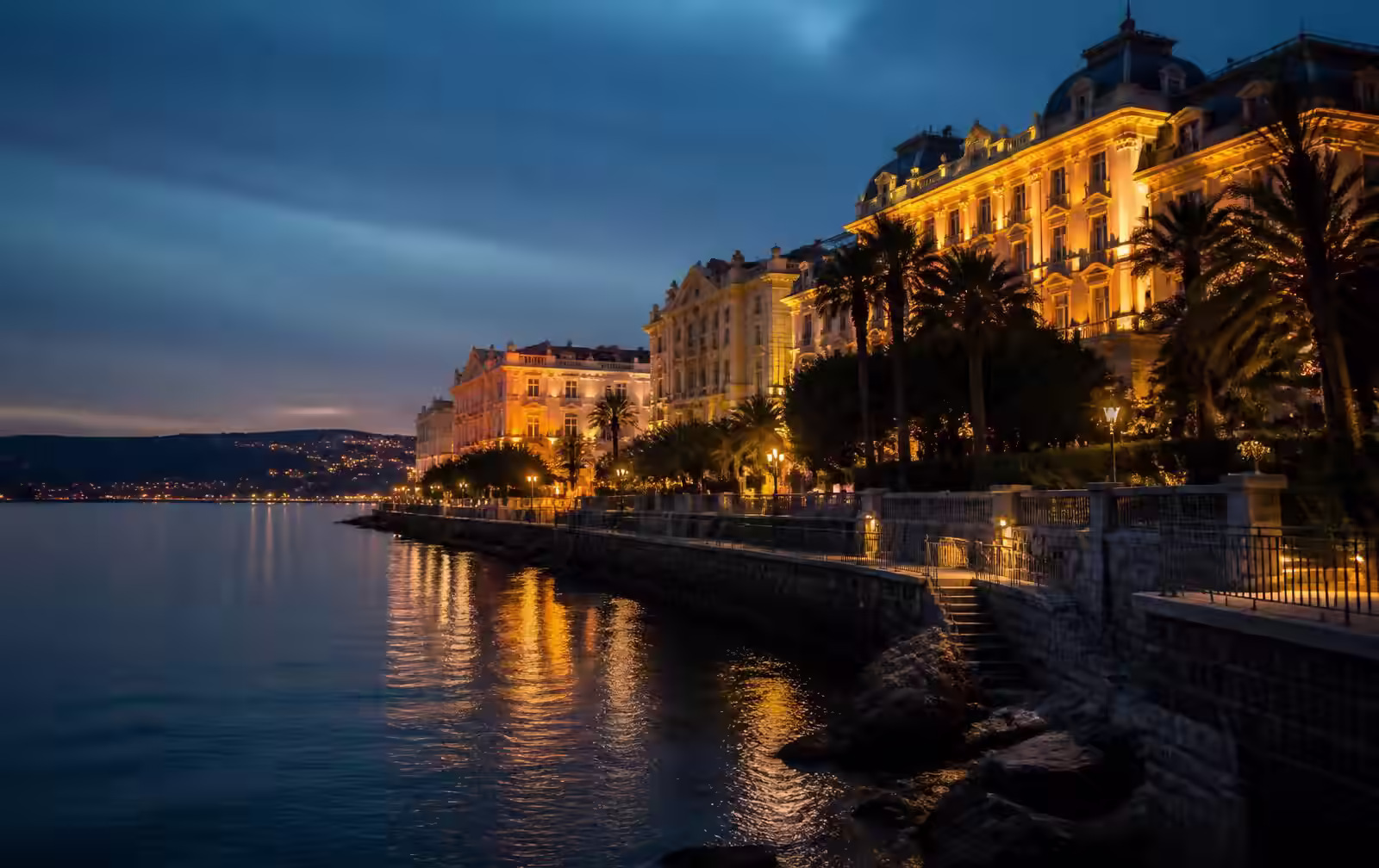 The Opatija riviera at night — a lamp-lit seaside promenade, grand historic façades and calm water under a dark sky