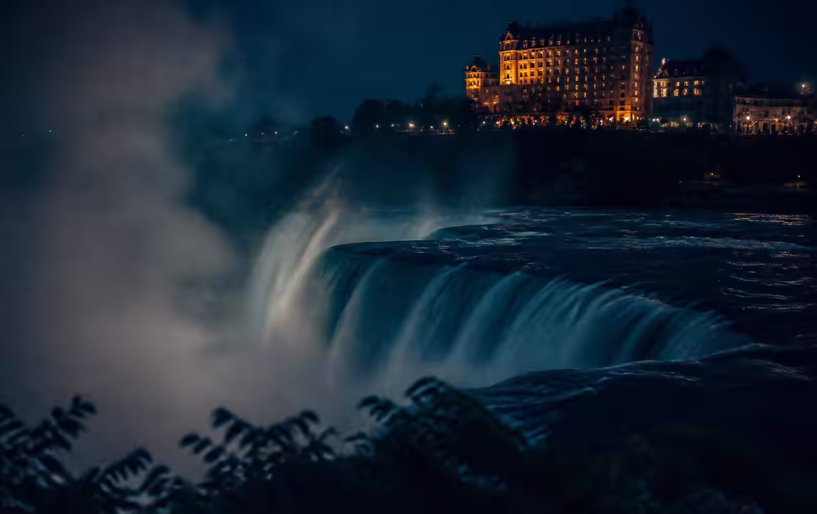 Night mist above dark falling water with distant warm hotel lights along the Niagara gorge