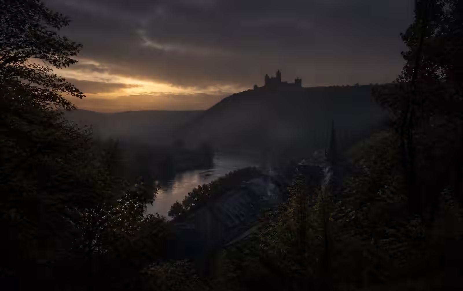 A wooded northern river valley at dusk with a distant castle silhouette on a ridge above a small town