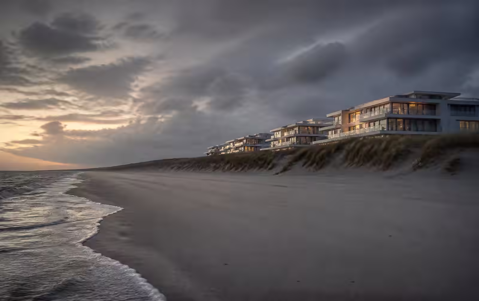 Wide North Sea beach at dusk with low dunes and elegant modern apartment terraces with lit windows set behind the dune line