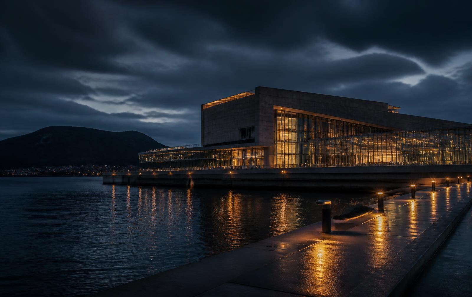 Northern Danish waterfront at night with a modern concrete and glass cultural building lit warmly above dark fjord water and an empty quayside