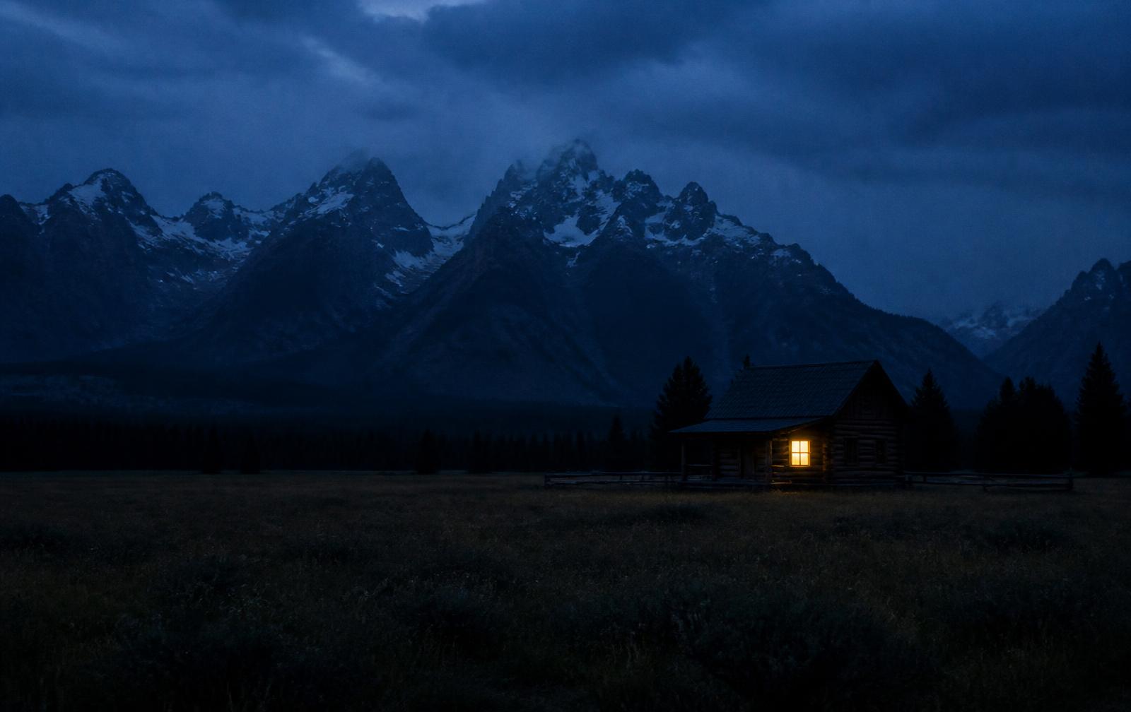 Alberta at night with prairie giving way to dark Rocky Mountain peaks and one warm lit window