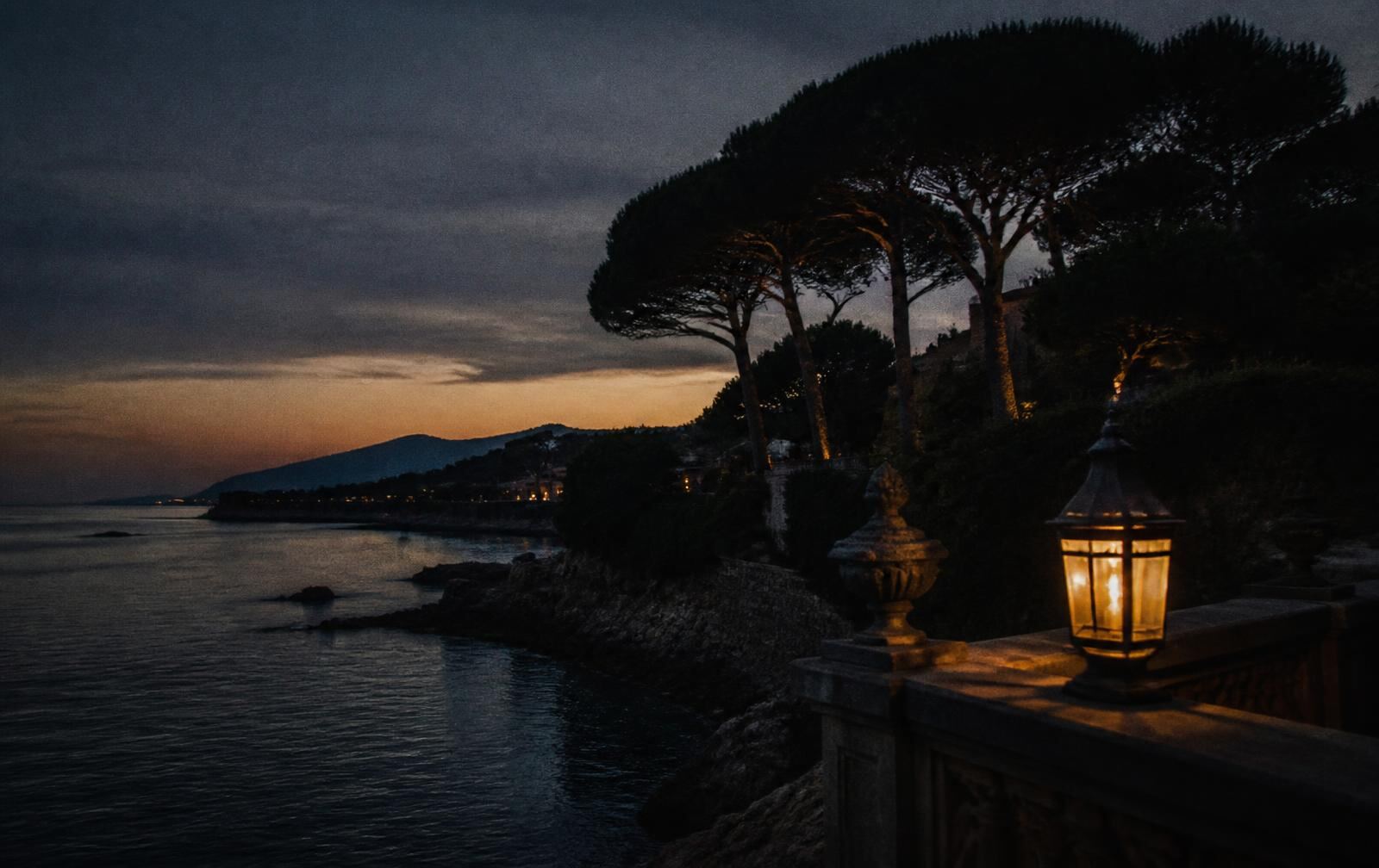 A lantern-lit stone terrace on the Cap d’Antibes coastline at dusk above a calm Mediterranean