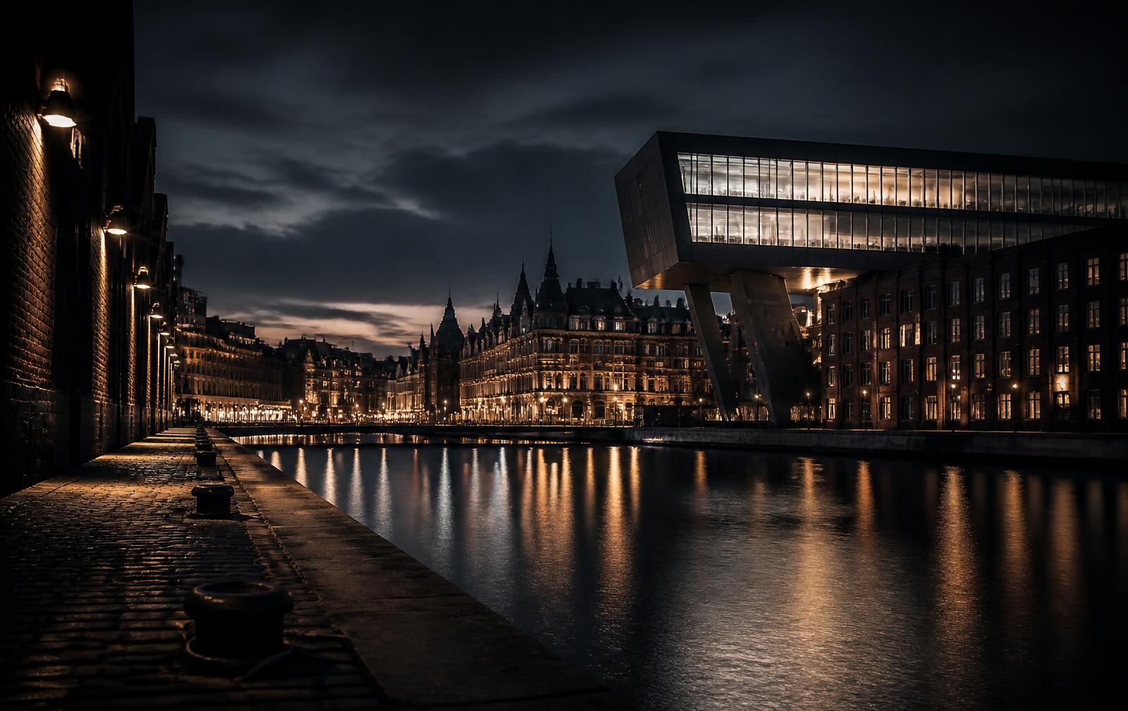 Antwerp river quay at night with historic warehouse façades, bold modern architecture and lights reflecting on dark water