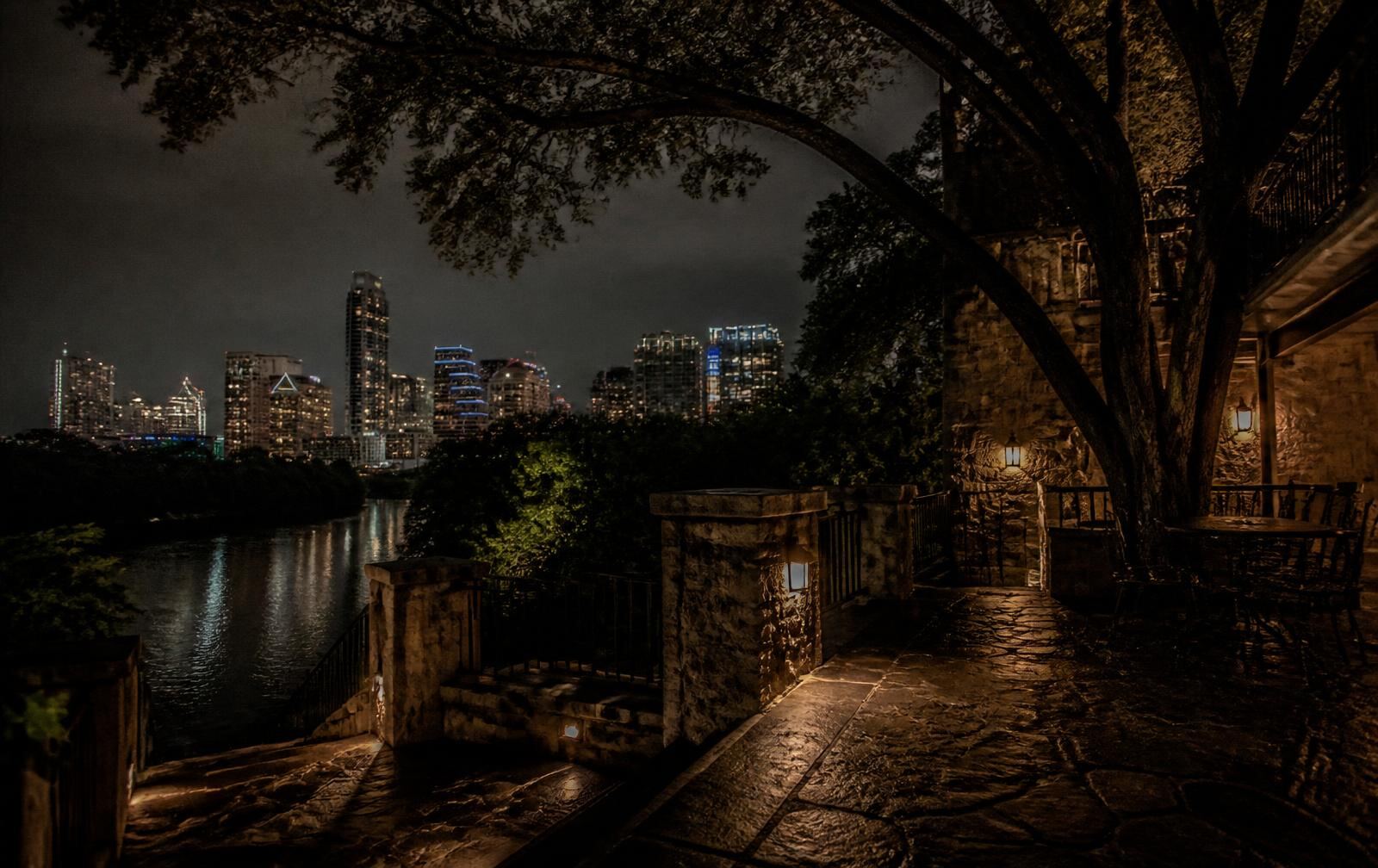 A quiet, dimly lit Austin loft interior at night with the downtown skyline glowing softly through a window